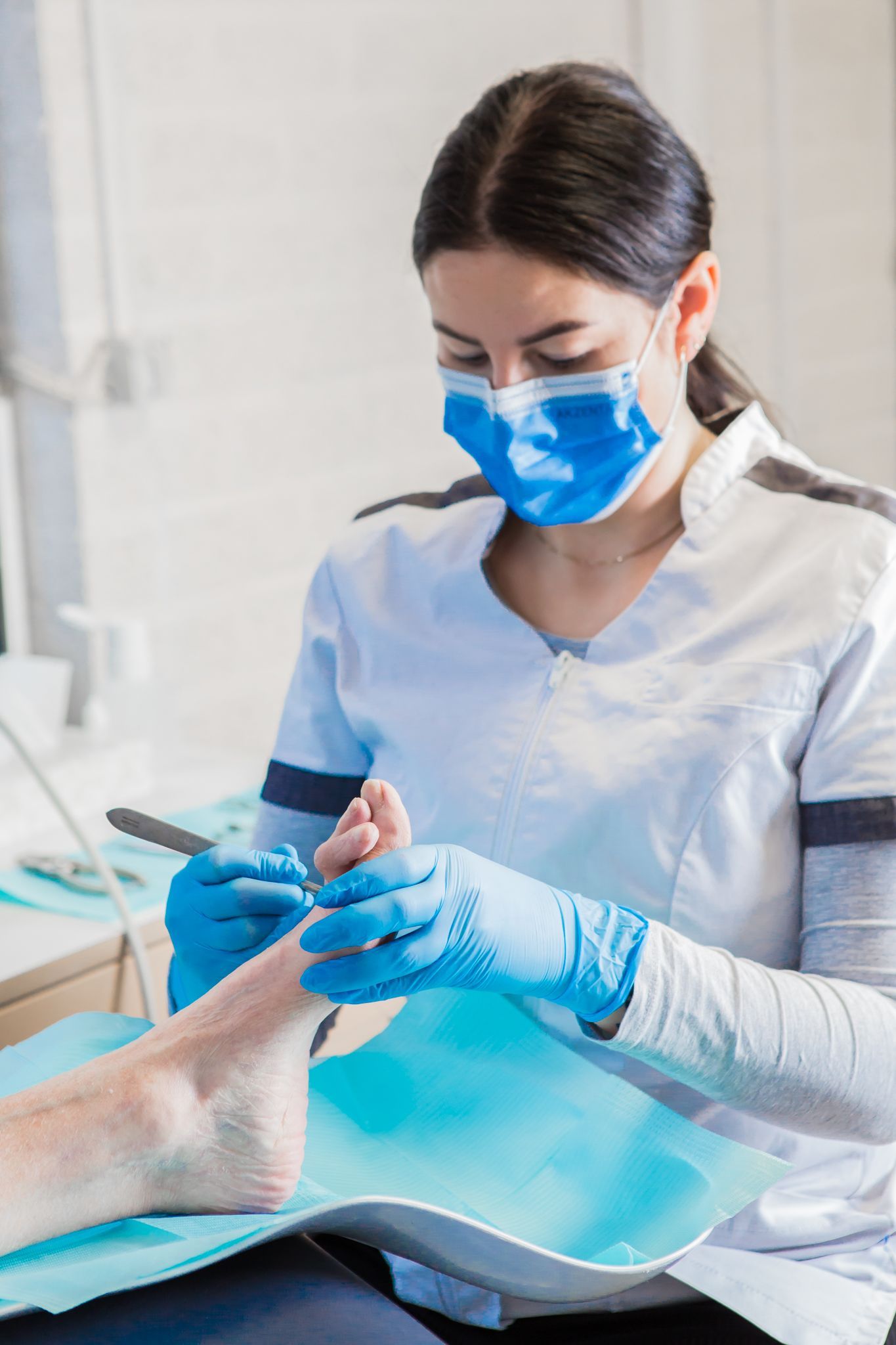 Een vrouw draagt ​​een masker en handschoenen terwijl ze de teennagels van een patiënt knipt.