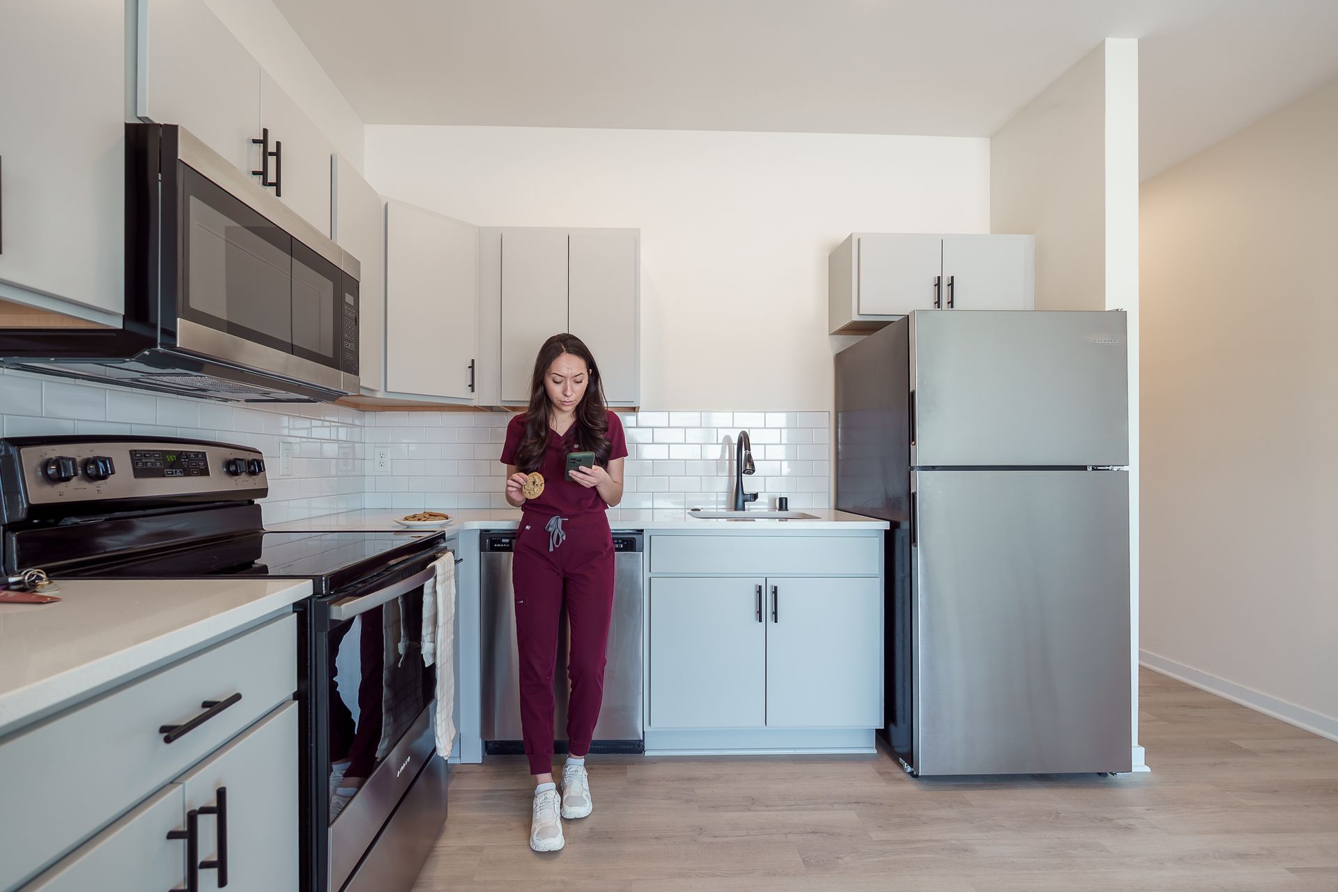 Photo of a woman wearing scrubs and standing in a kitchen using a digital device