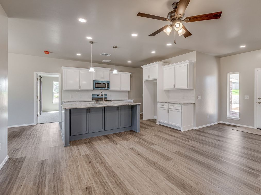 Open-concept kitchen with white cabinets, gray island, light wood floors, and ceiling fan.