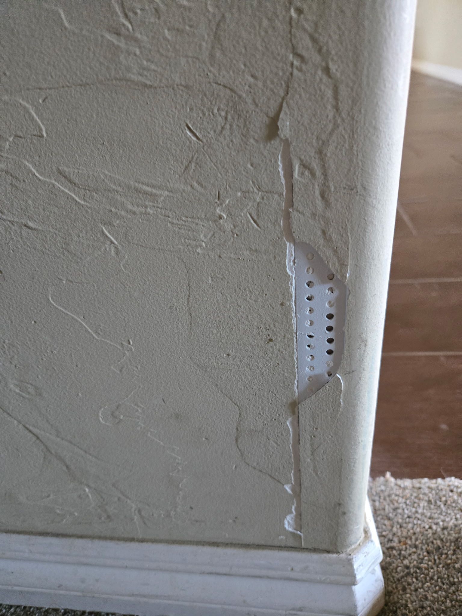 Damaged stucco wall revealing a white plastic vent.