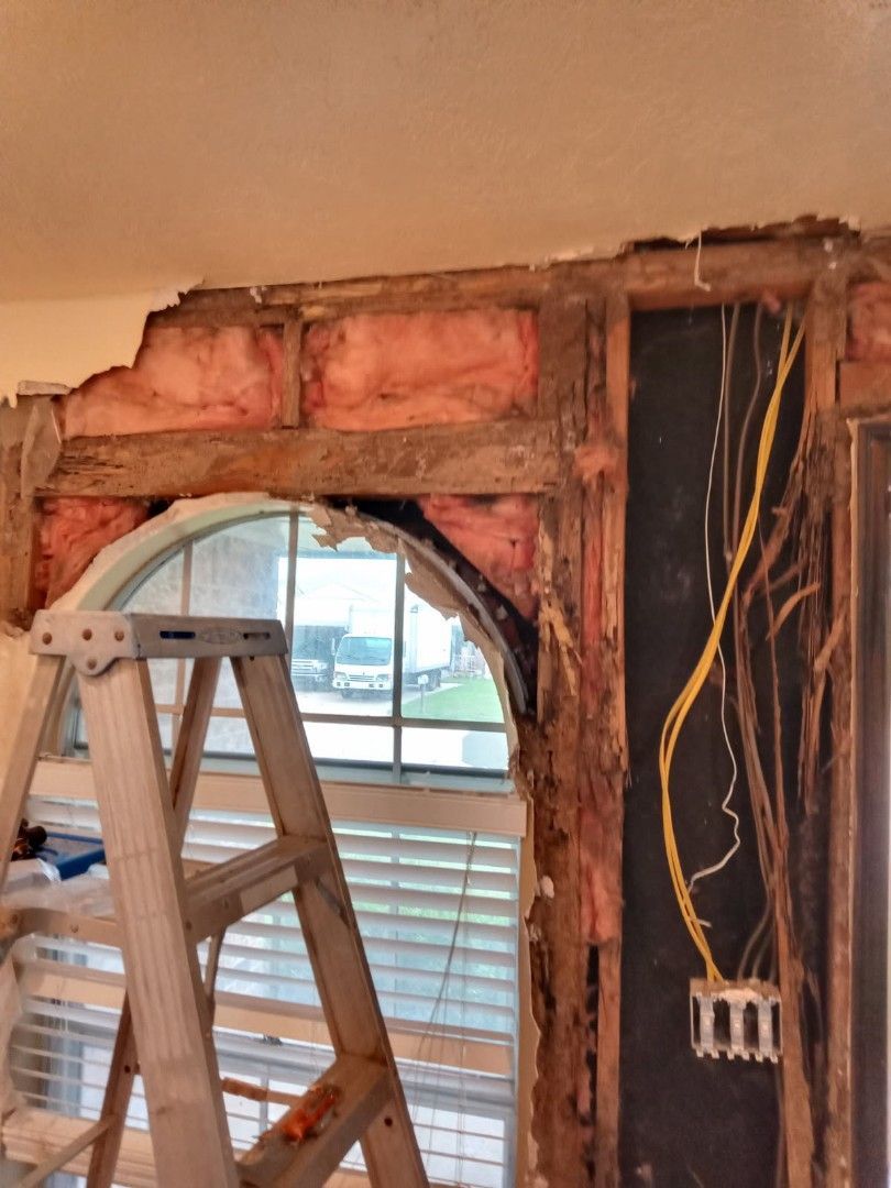 Interior wall under construction showing insulation, electrical wiring, and arched window. Ladder in front.