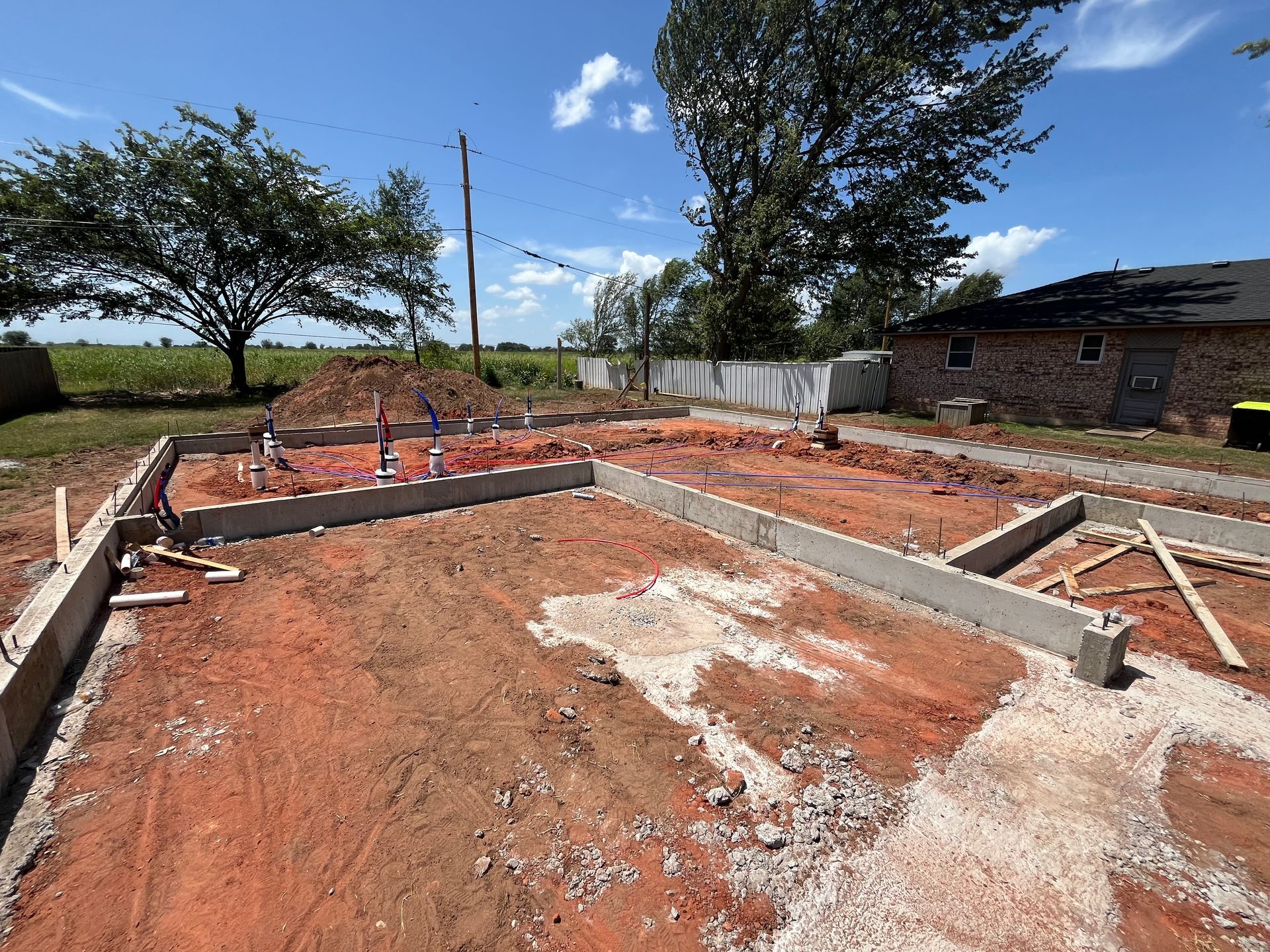 Construction site with concrete foundation and plumbing lines against a blue sky.