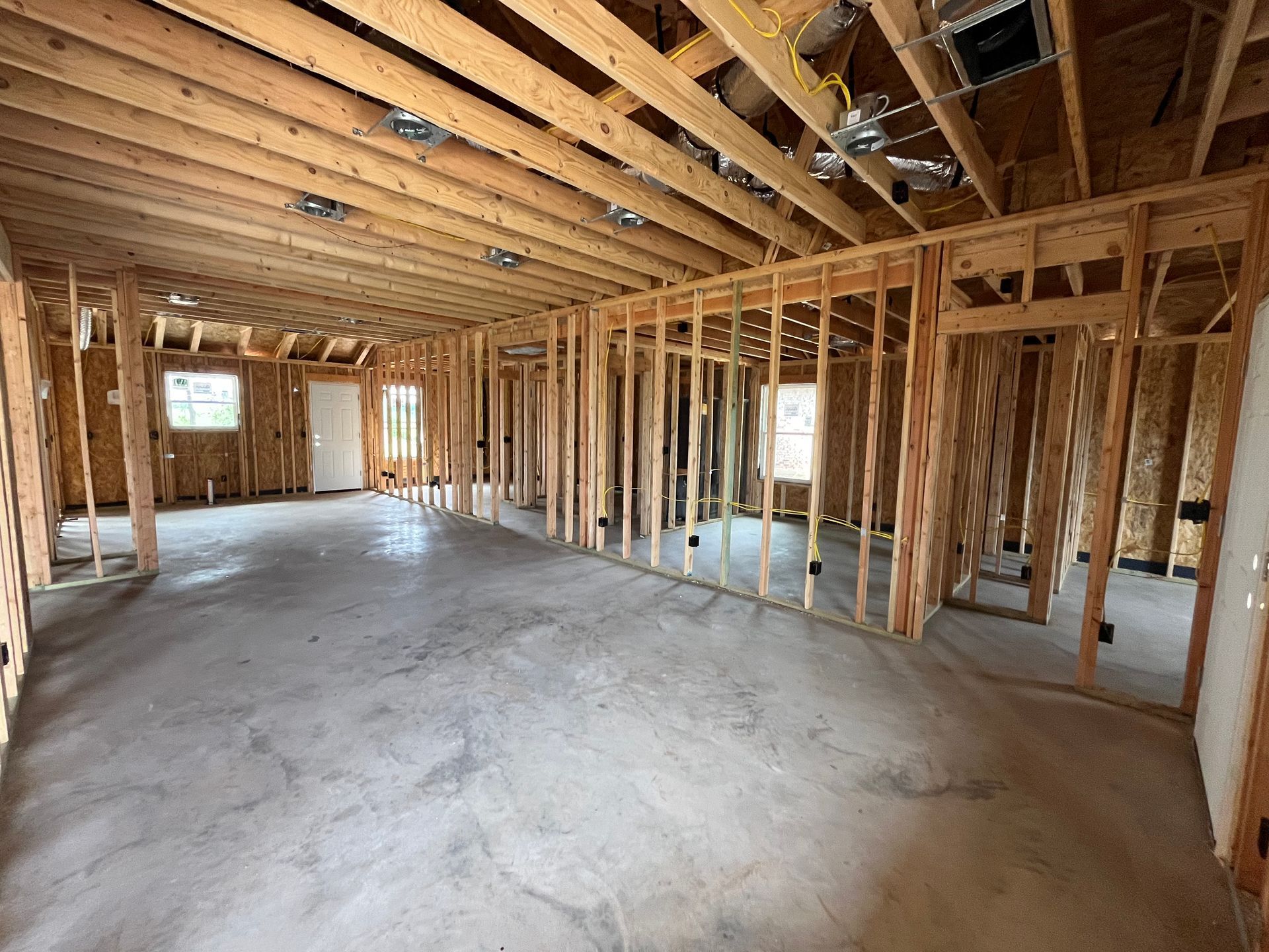 Interior view of a new construction home's framing. Stud walls, exposed beams, and concrete floor.