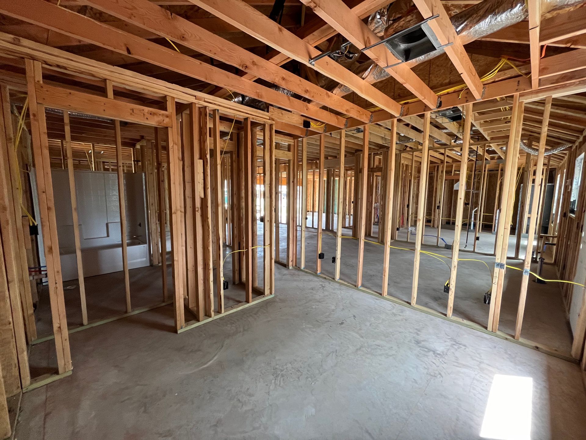 Interior of a building under construction, showing wooden studs framing walls and ceiling; concrete floor.