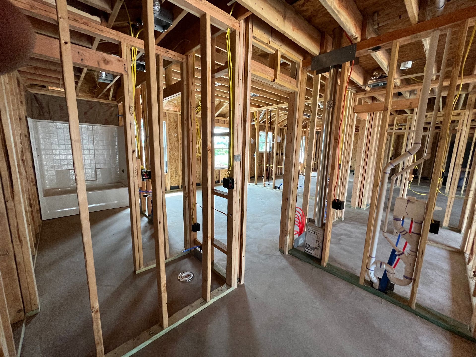 Interior of a house under construction; wooden framing, concrete floors, visible electrical and plumbing.