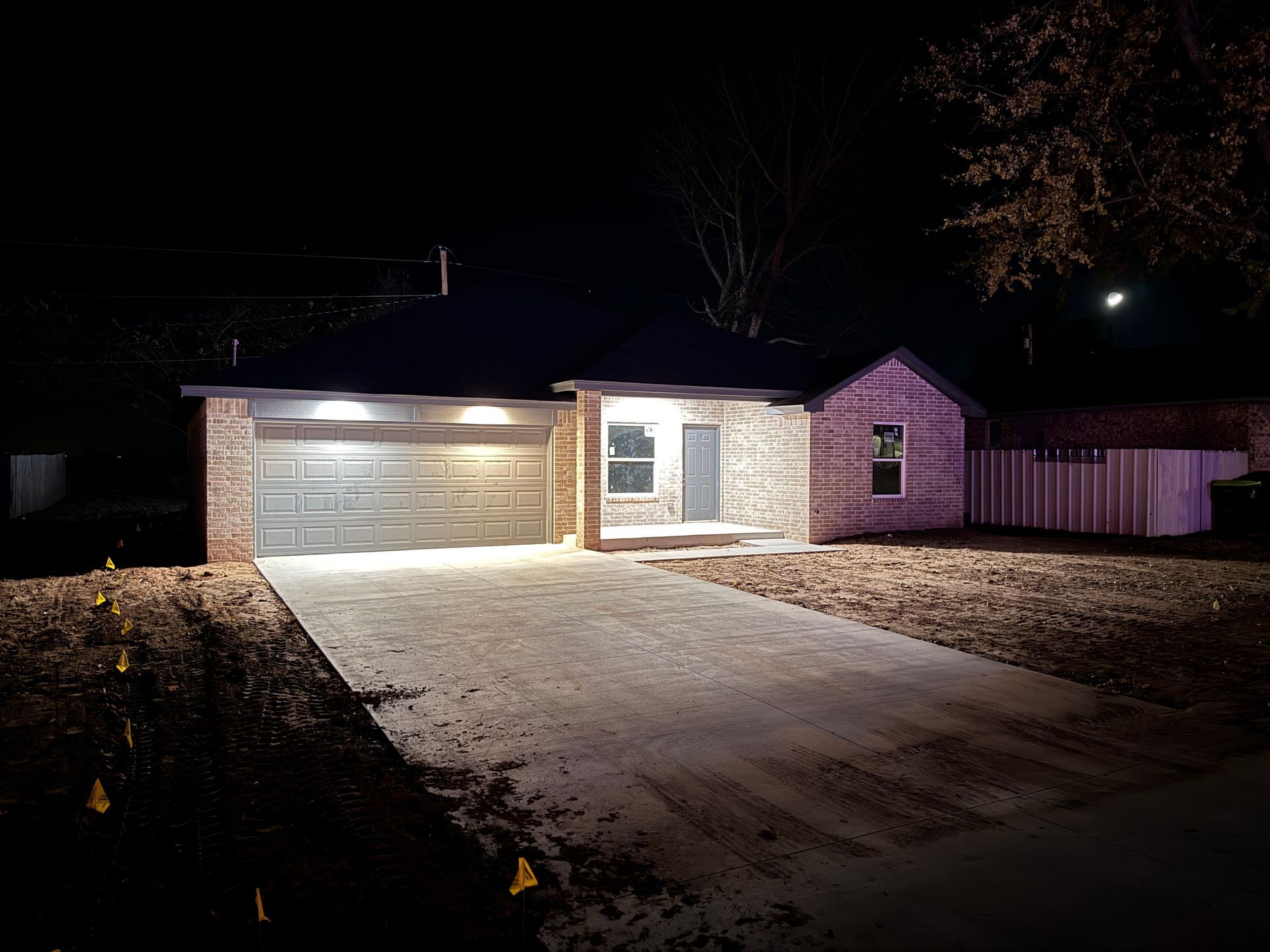 Nighttime view of a brick house with a garage and driveway. Exterior lights illuminate the front of the home.