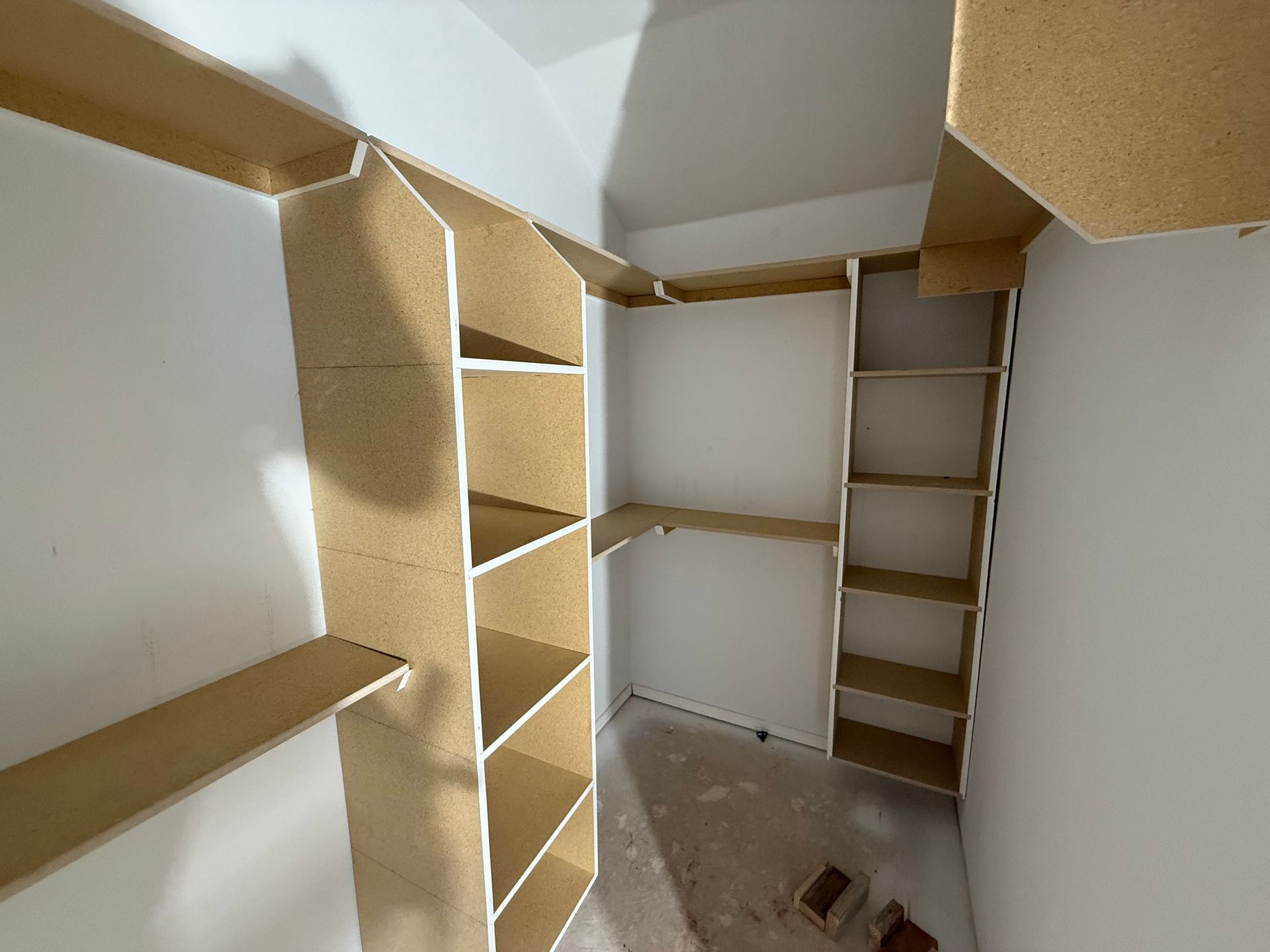Custom-built closet with shelving units constructed from light-colored wood. Shelves are against white walls in an unfinished space.