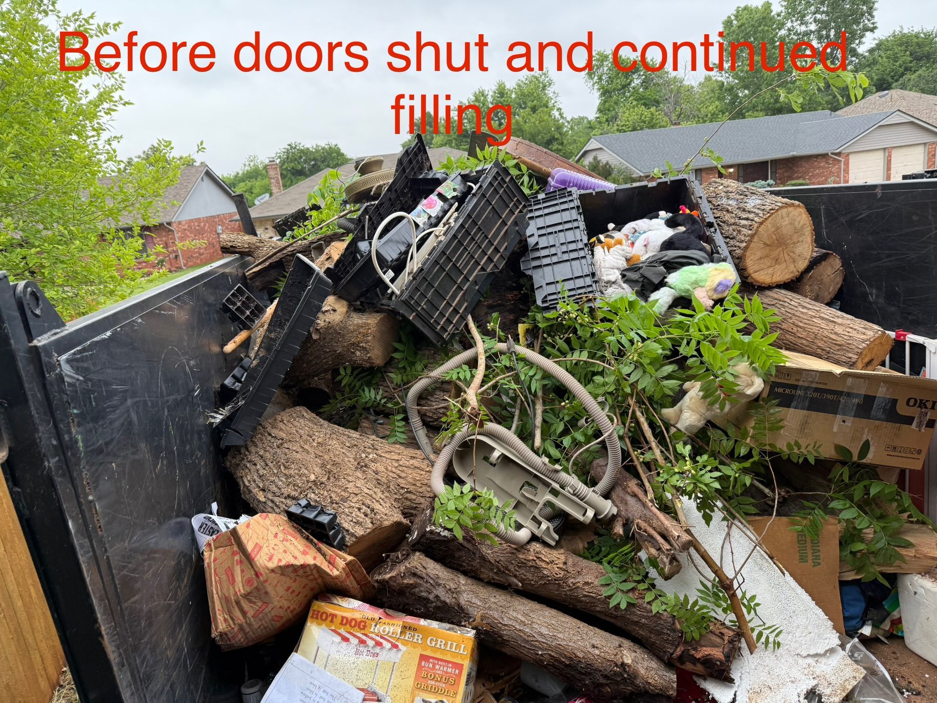 Dumpster overflowing with logs, greenery, and debris, before the doors closed.