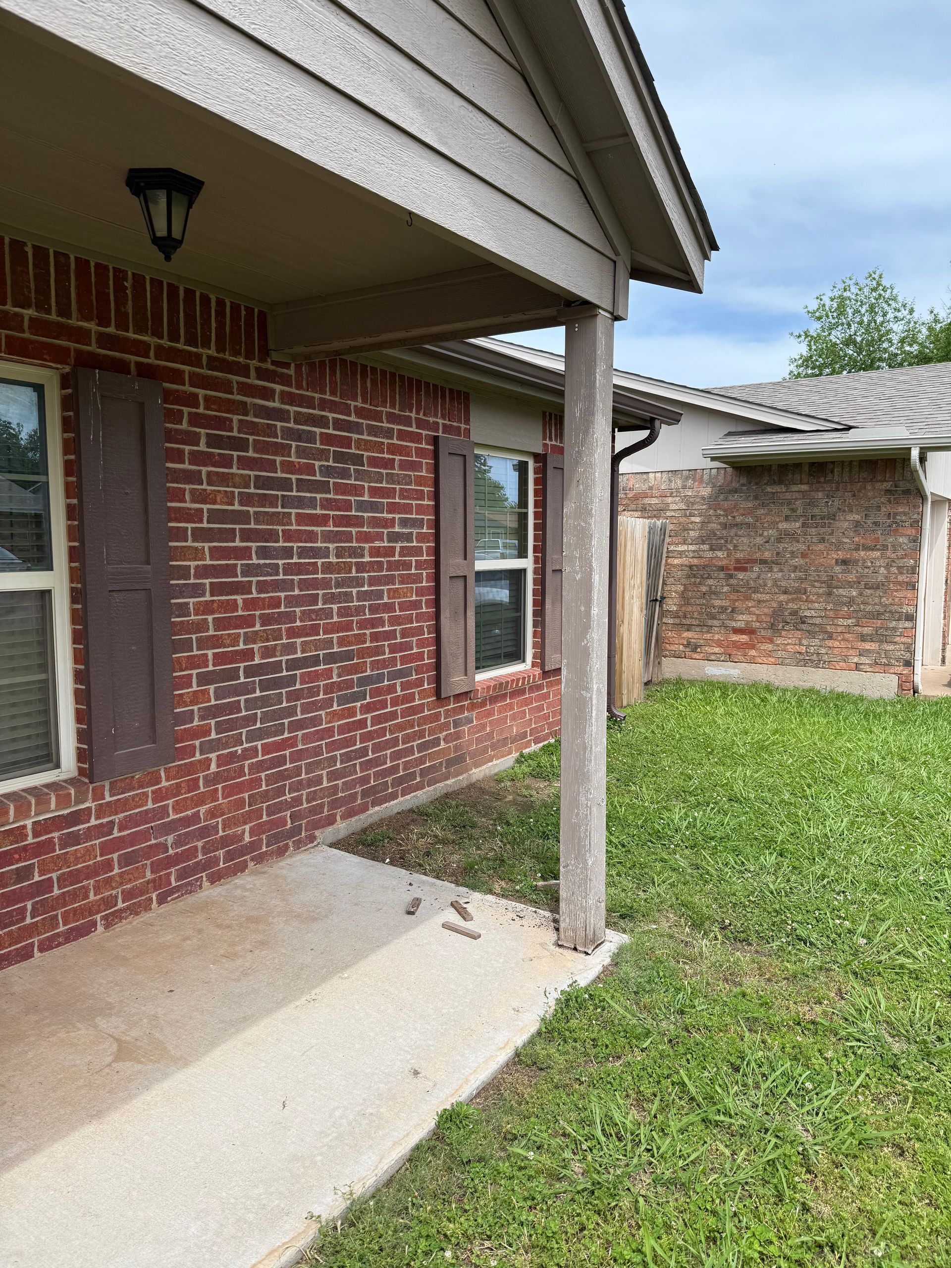 Brick house with concrete porch and grass yard. Brown shutters, tan trim, and a cloudy sky.