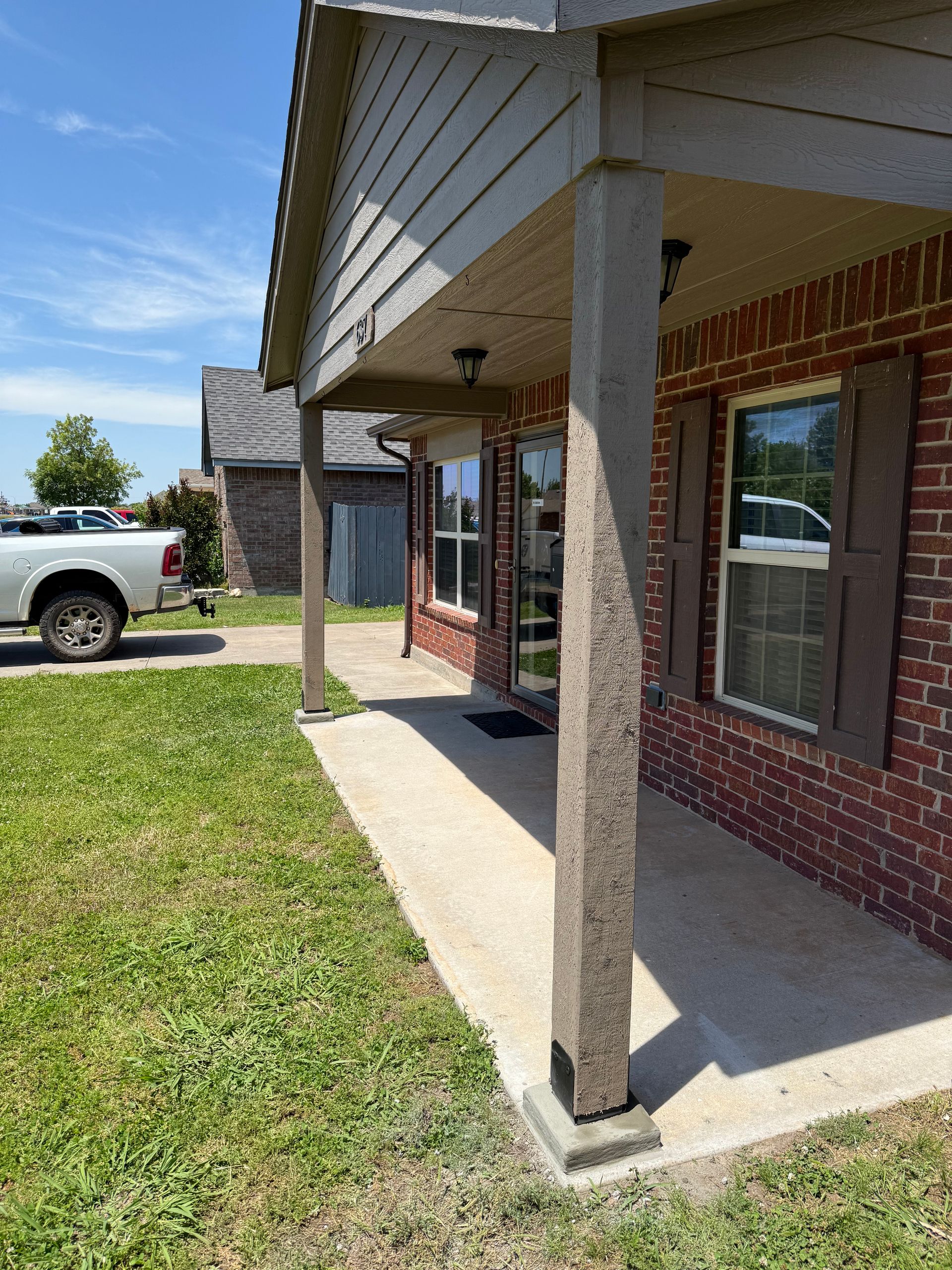 Front porch with concrete columns, brick house, and green grass.