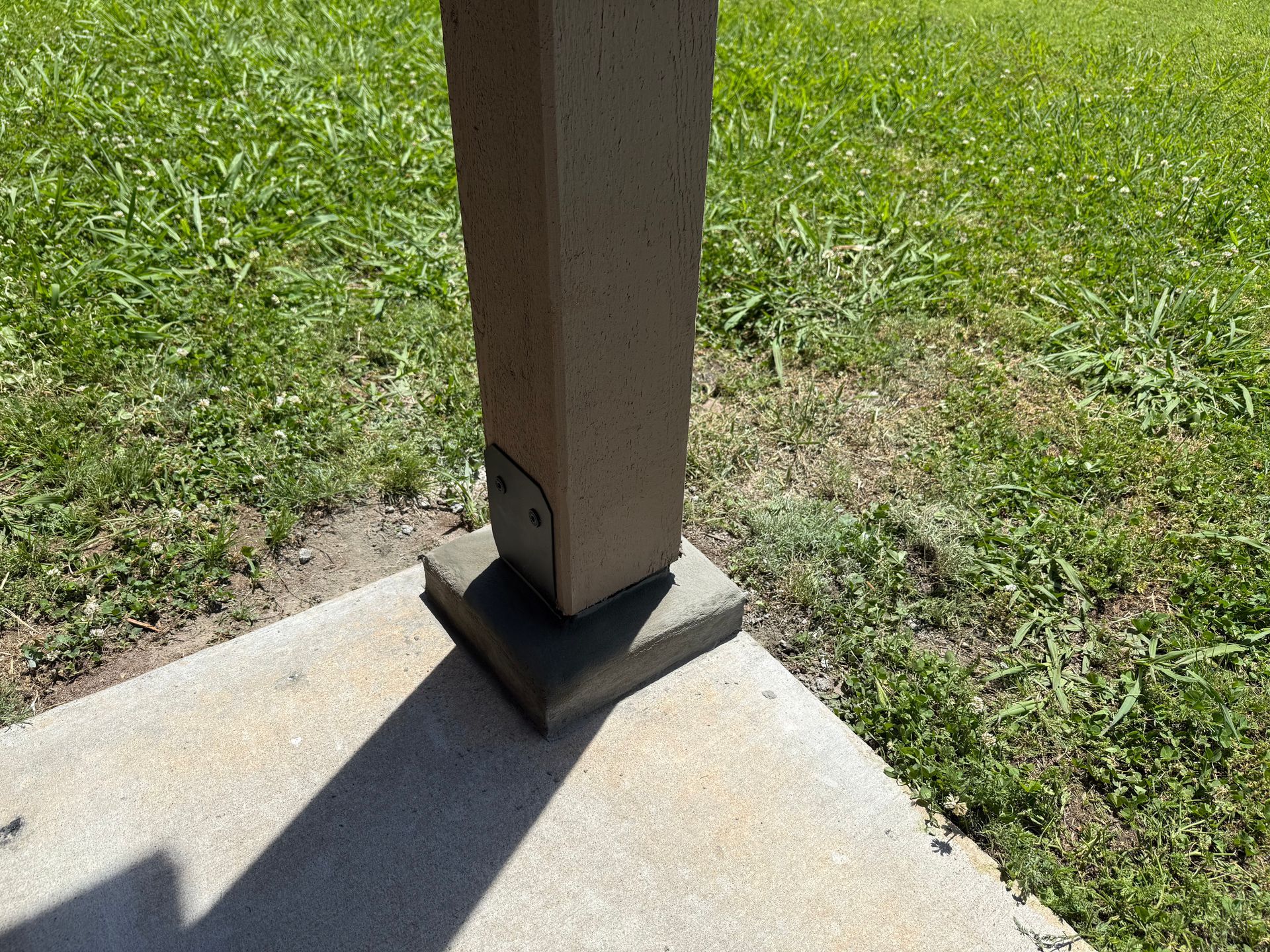 Beige square pillar on a concrete base, set on a concrete patio. Green grass surrounds.