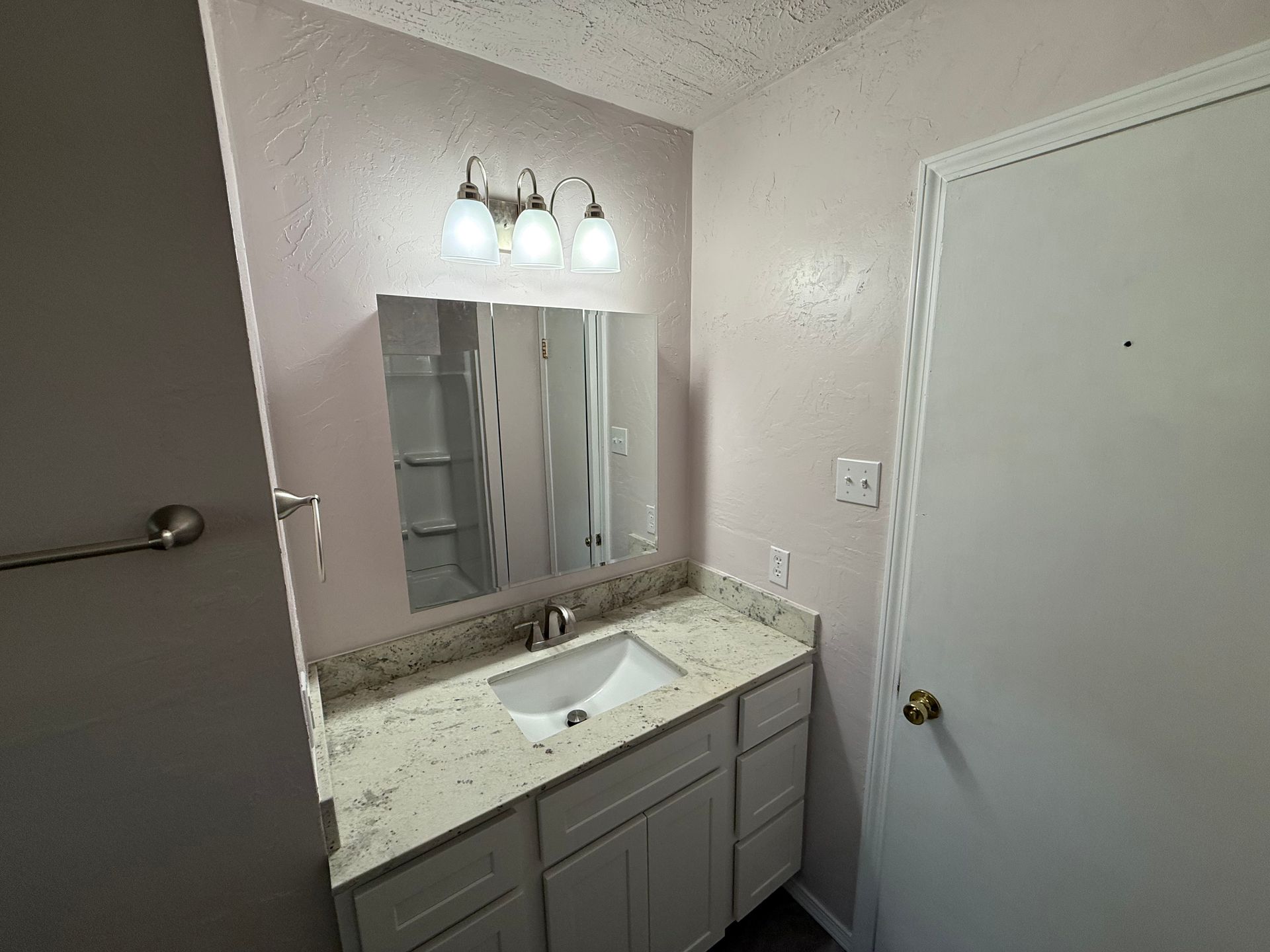 Bathroom with white vanity, speckled countertop, and wall mirror. Door on the right.
