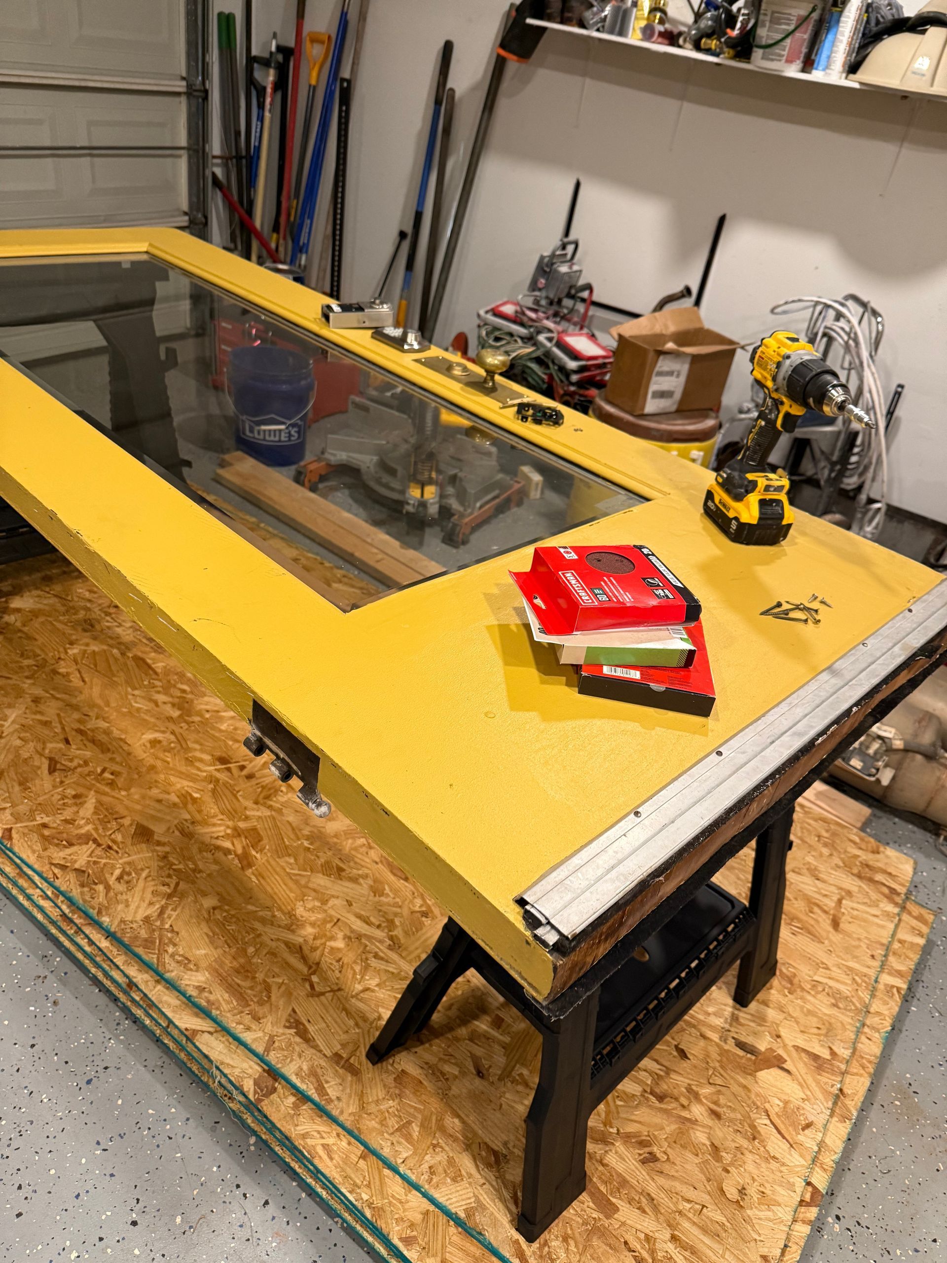 A yellow door with glass, on a work table in a garage. Tools and materials are nearby.