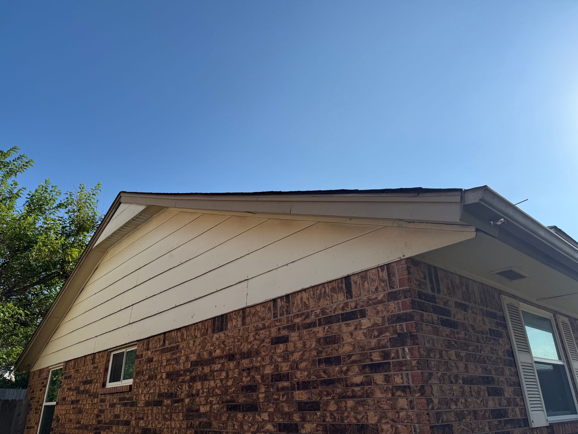 Brick house with white siding and dark roof under a clear blue sky.