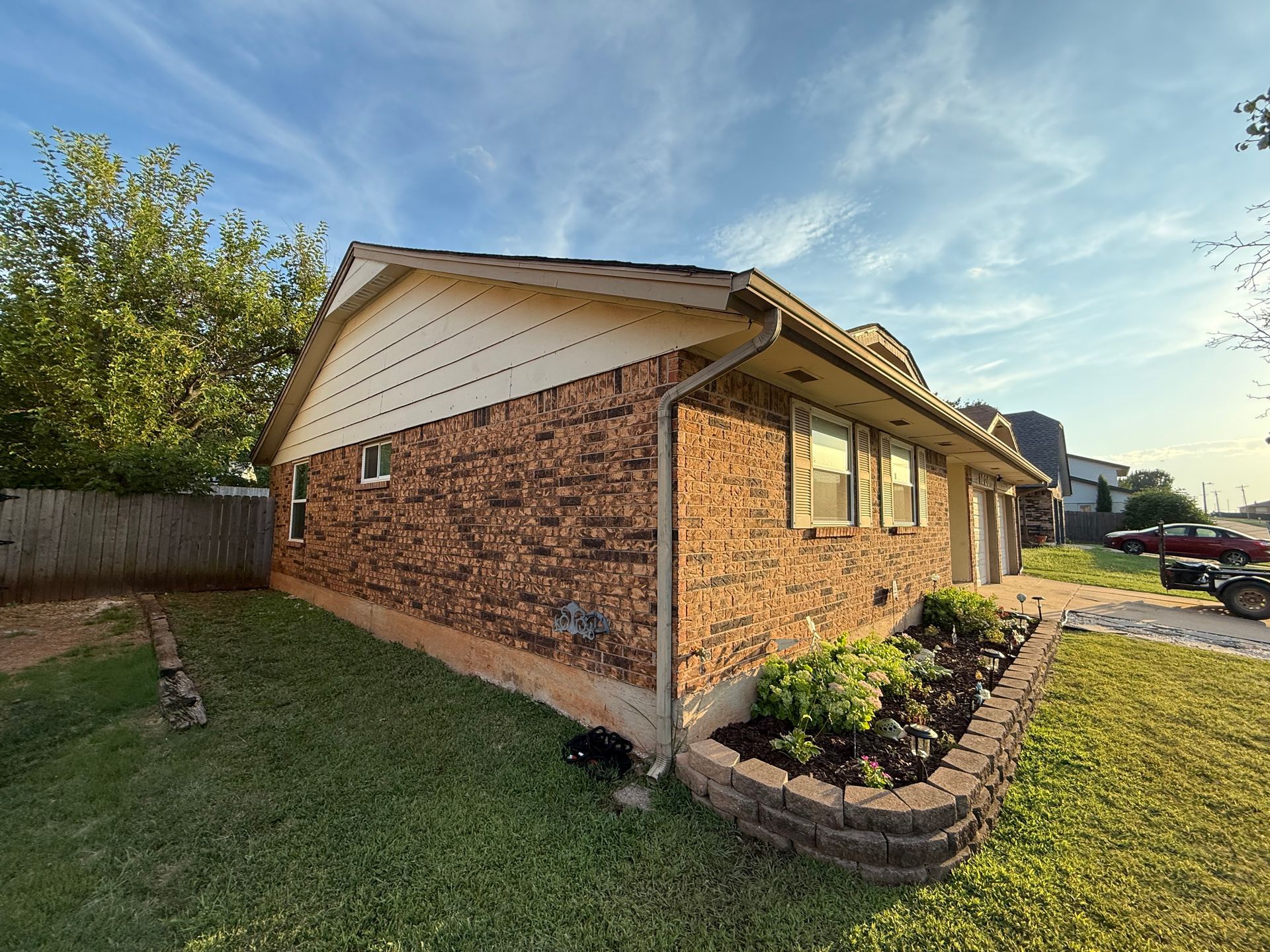 Brick house with tan trim, small garden bed, and green lawn. Blue sky.