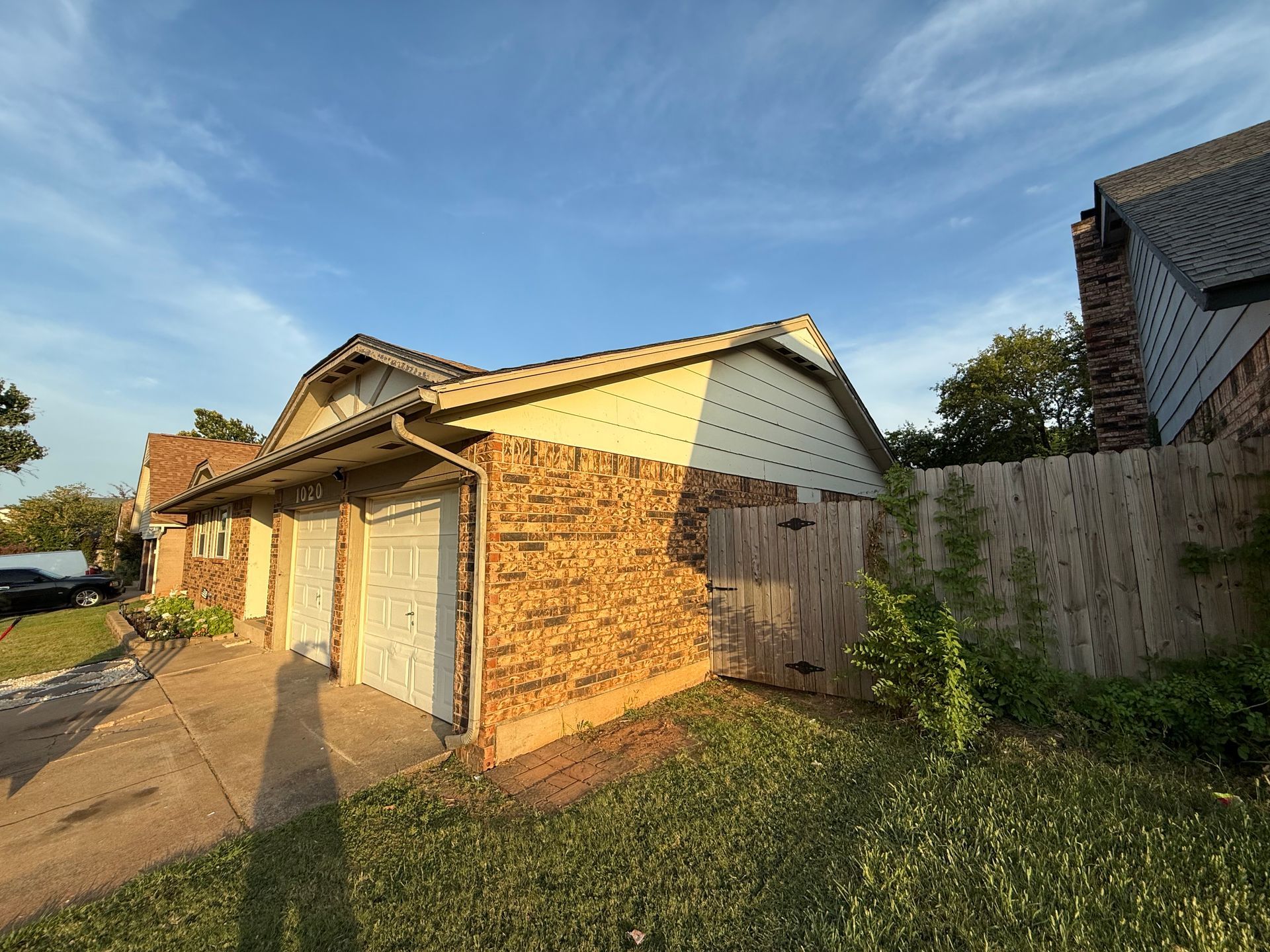 Brick townhouse with two garage doors, wooden fence, and blue sky.