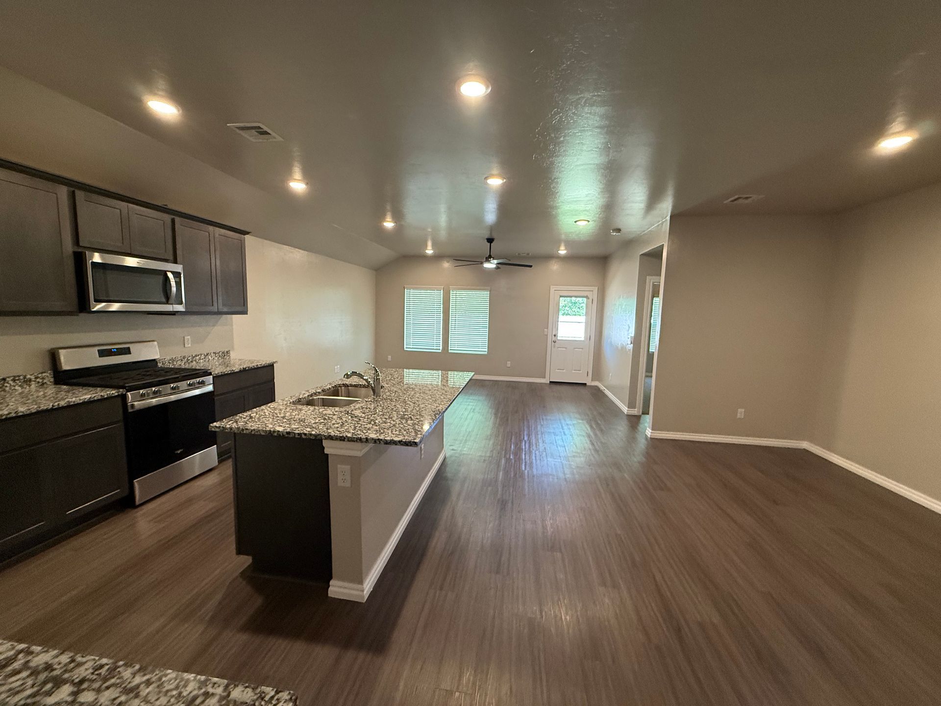 Modern kitchen with gray cabinets, granite countertops, and dark wood floors.