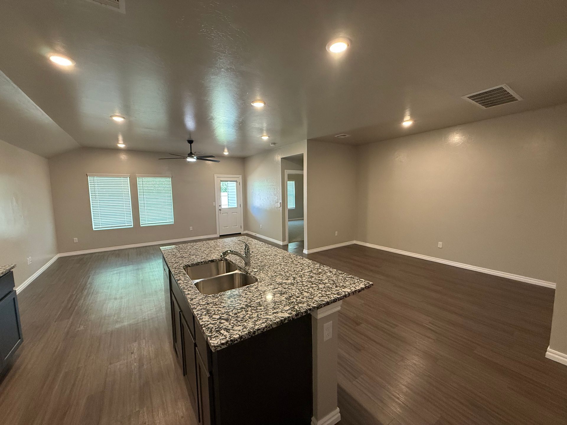 Open-concept kitchen and living area with island, dark cabinets, and wood-look flooring.
