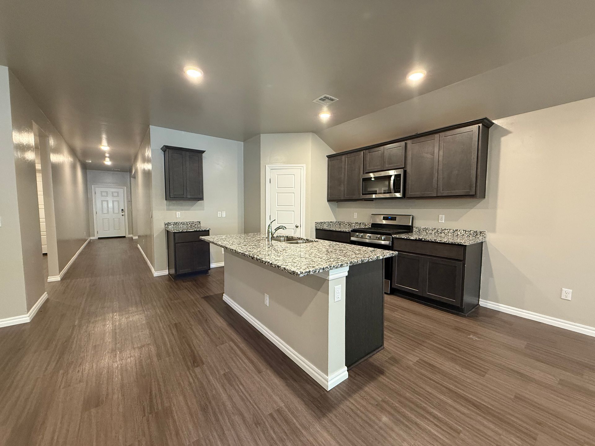 Kitchen with island and dark cabinets, granite countertops, and hardwood floors.