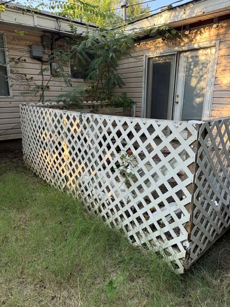 White latticework fence in front of a beige building with a glass sliding door. Green grass surrounds.