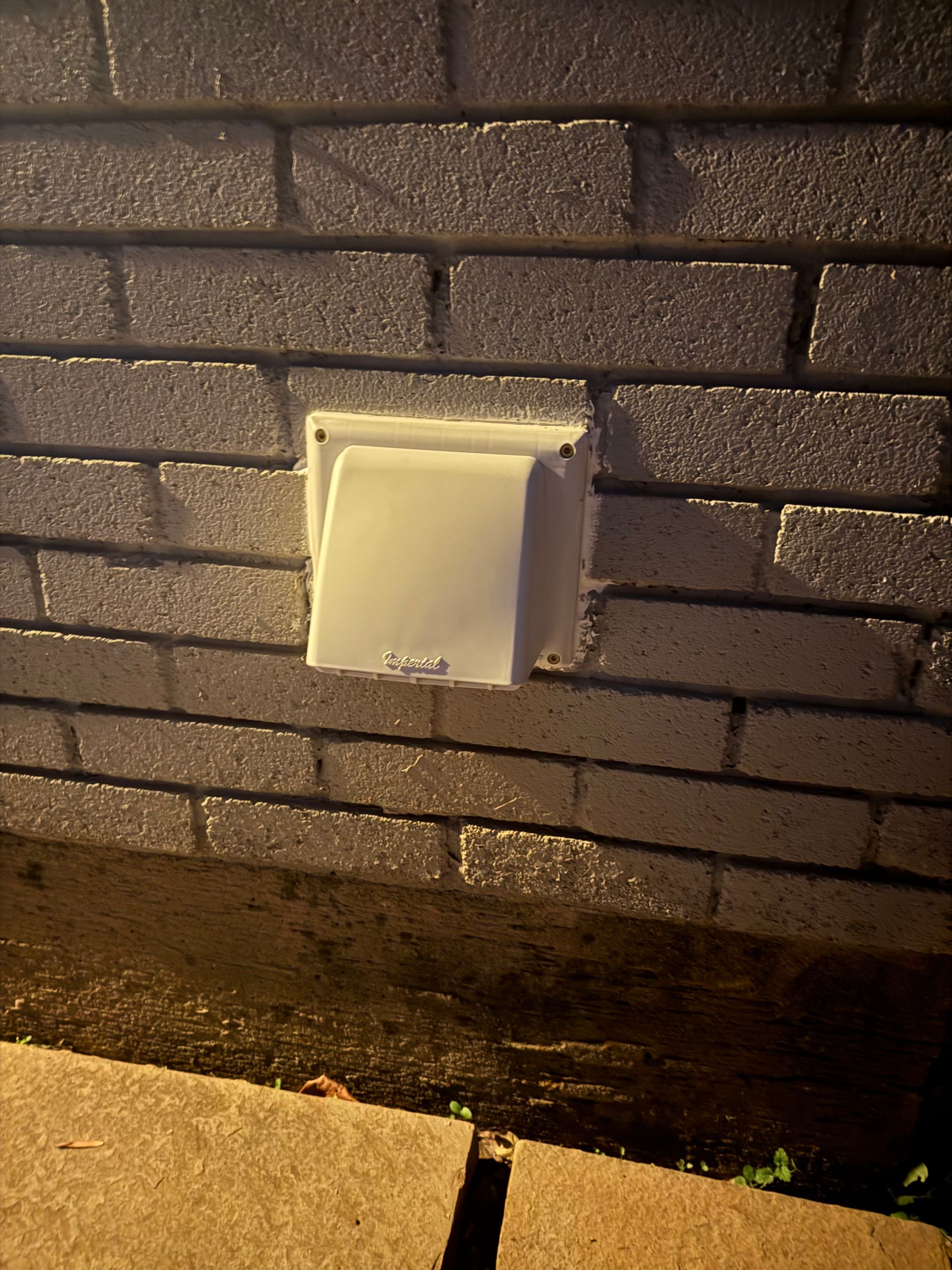 White vent cover on a brick wall, near ground level.