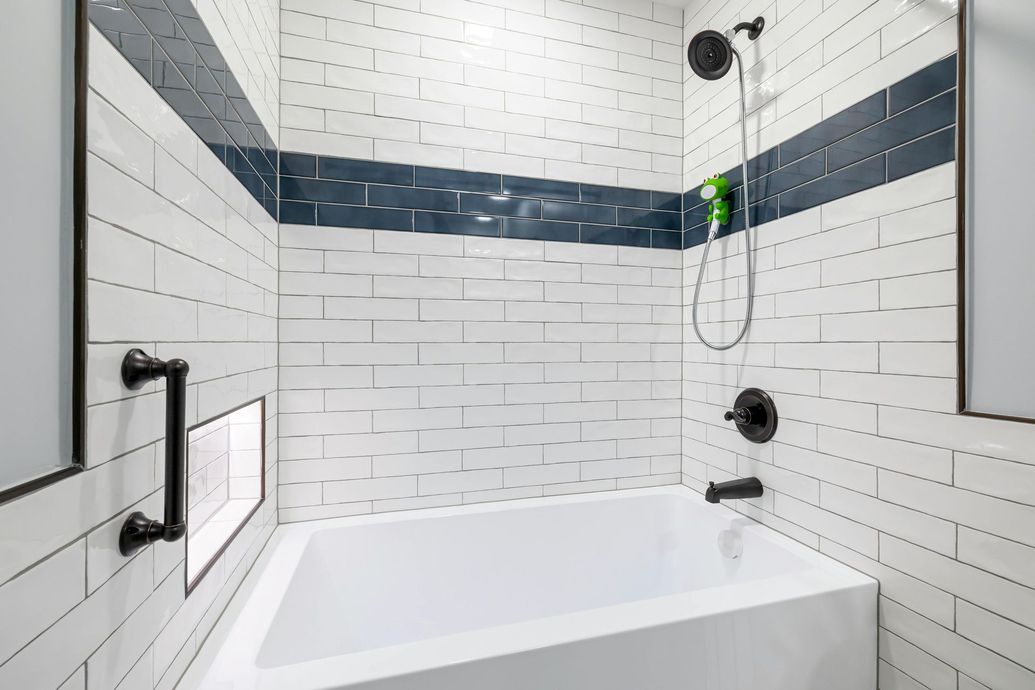 A white-tiled bathroom with a bathtub, black fixtures, and a dark blue accent stripe.