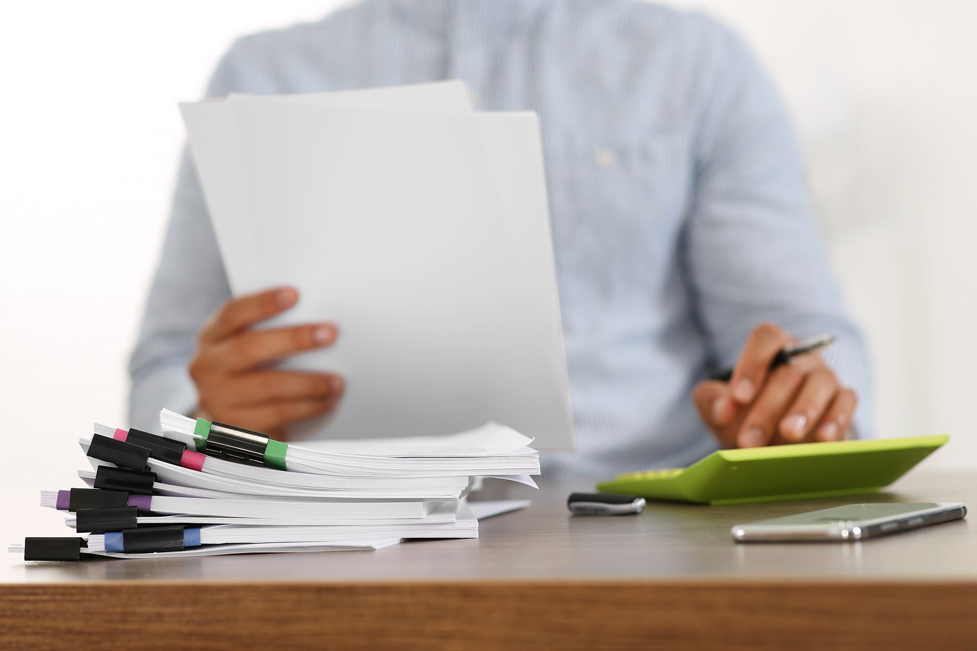 A man is sitting at a desk holding a piece of paper and using a calculator.
