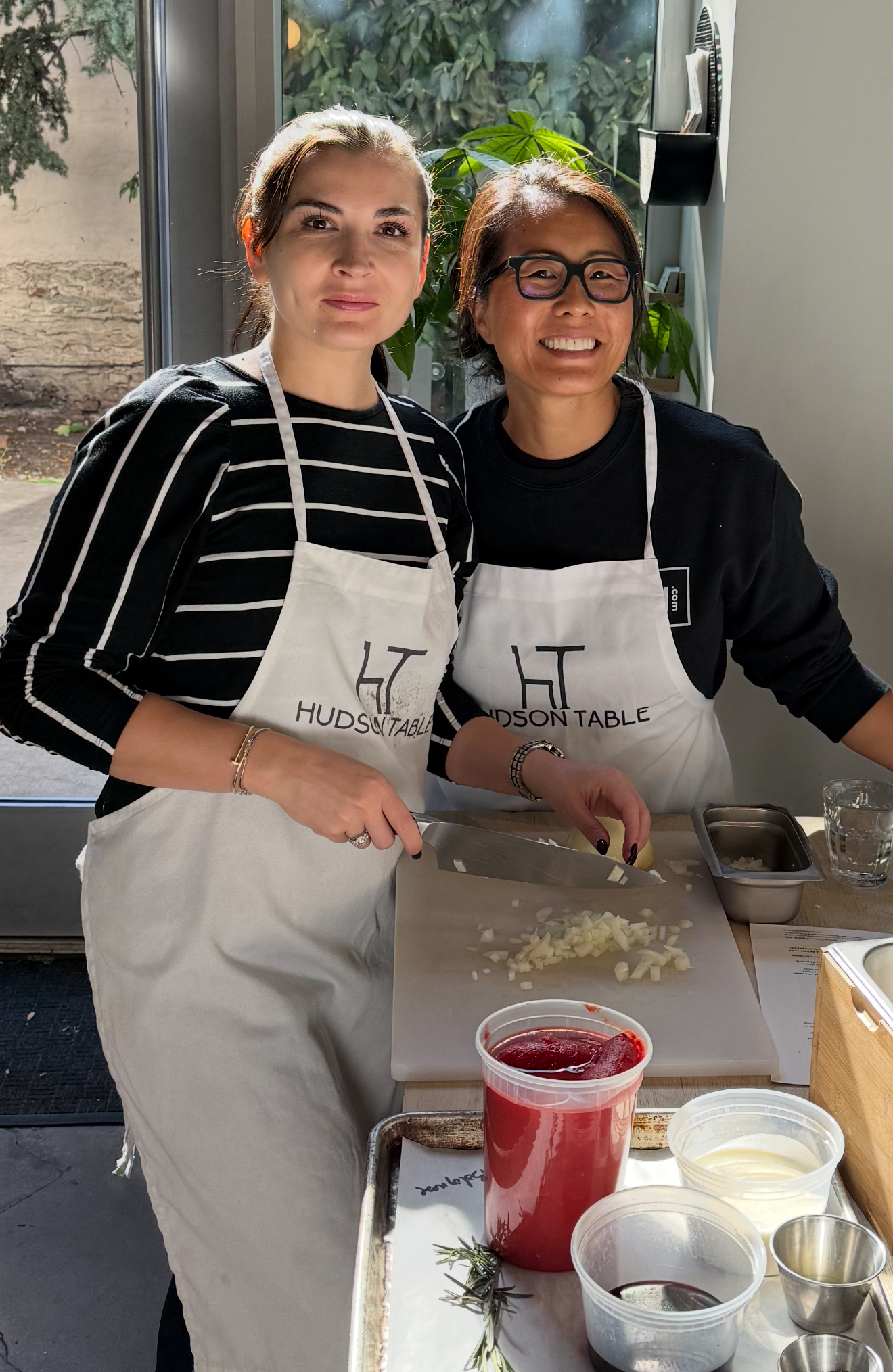 Two women wearing aprons are standing next to each other in a kitchen.