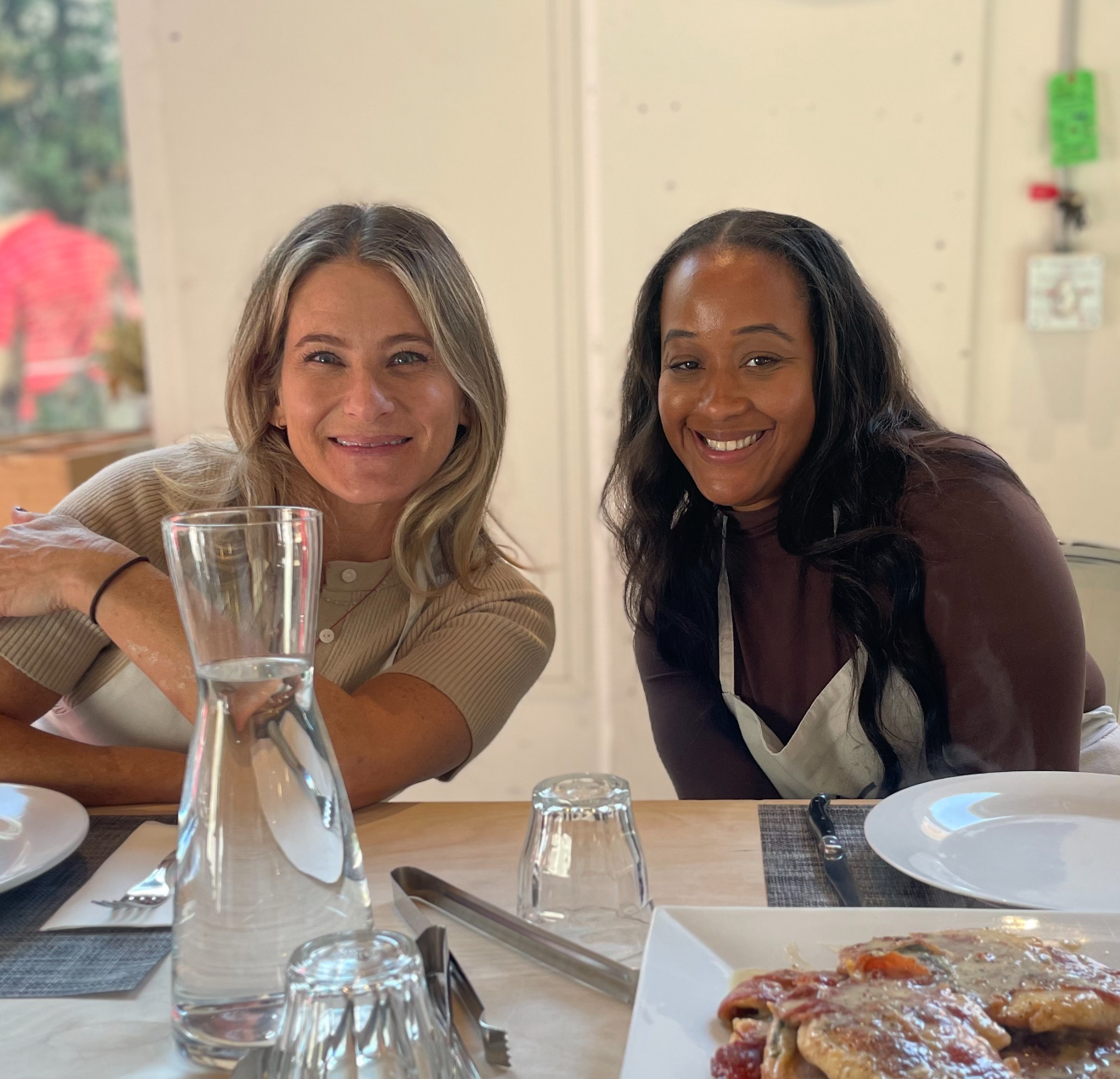 Two women are sitting at a table with plates and glasses