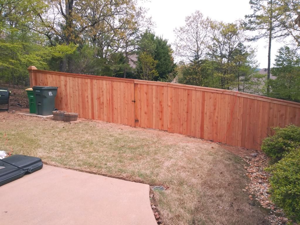 Wooden fence on a slight hill, with green grass and trees in the background.