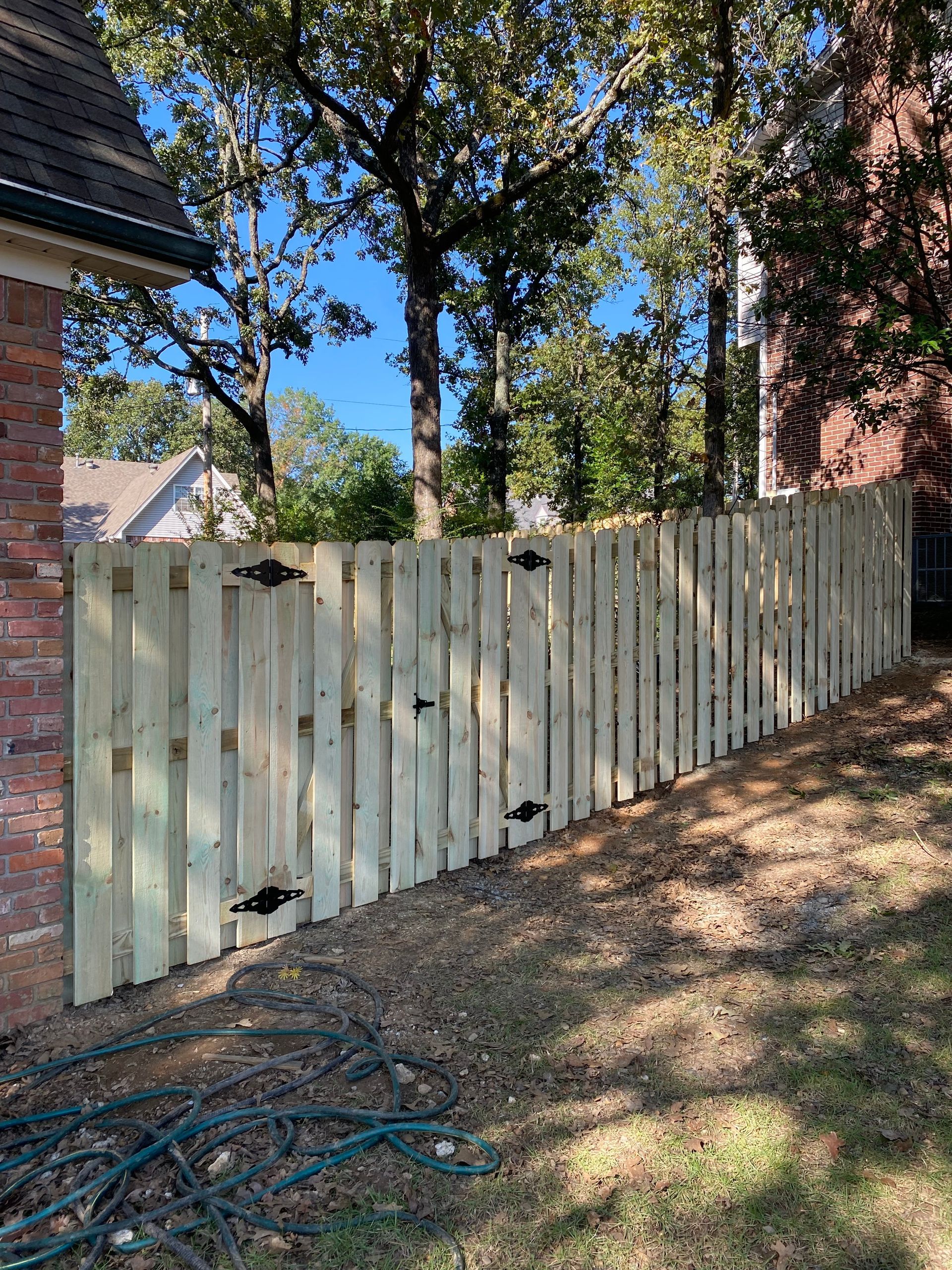 A wooden fence along a yard, next to a brick building. Trees and a blue sky in the background.