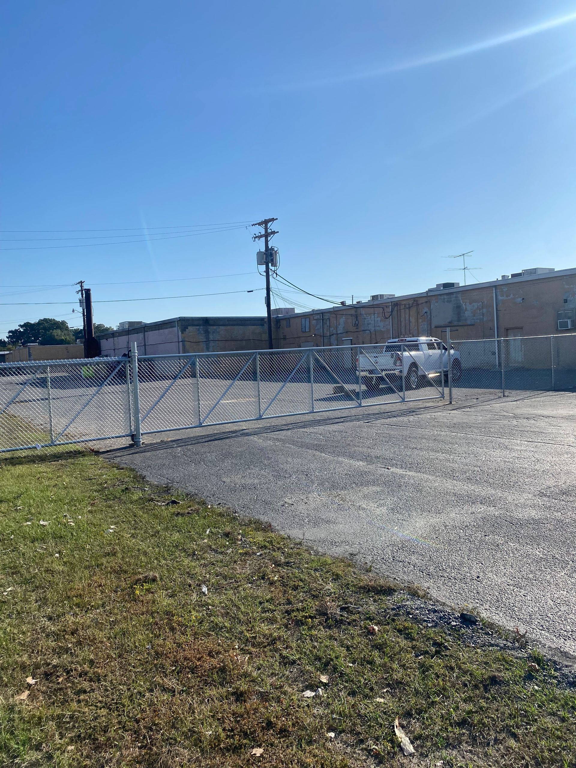 Chain-link fence in front of a gravel lot and building under a blue sky.