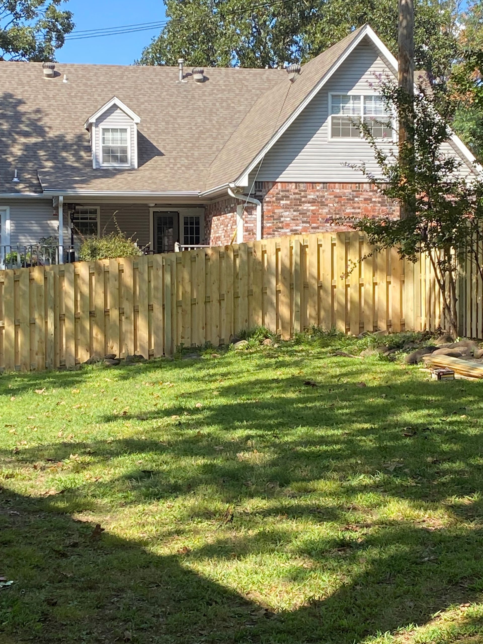 Wooden fence in front of a house with brick and gray siding. Green grass fills the yard.