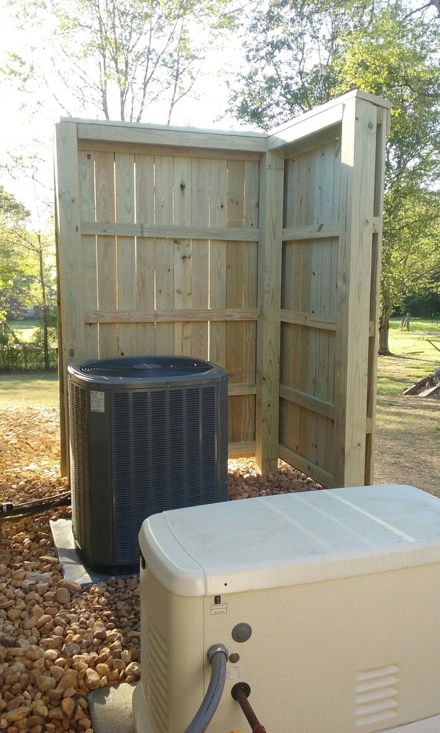 Air conditioner and generator next to a wooden privacy screen outdoors.