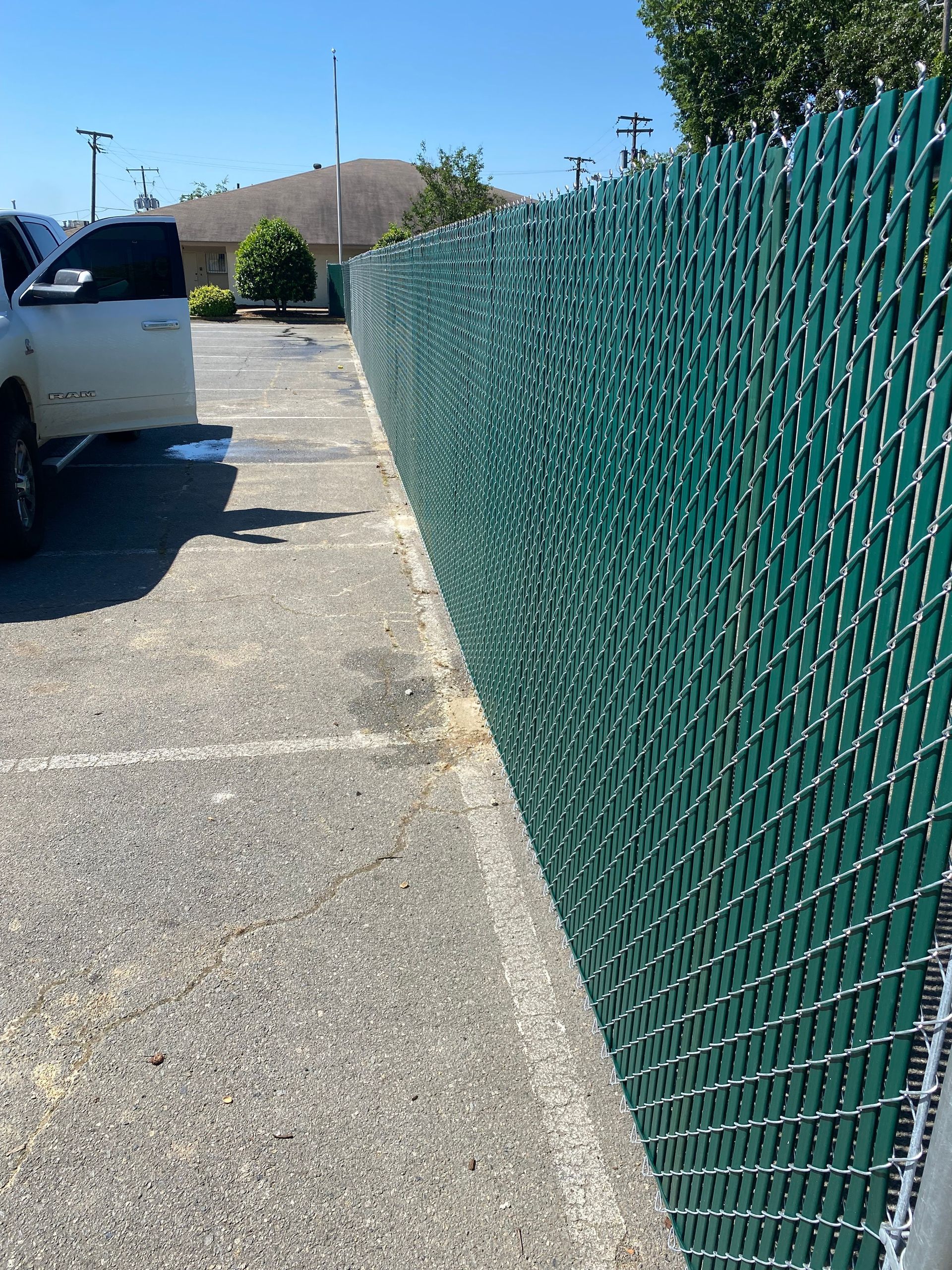 Green chain-link fence running along the edge of a parking lot. A white pickup truck is parked on the left.