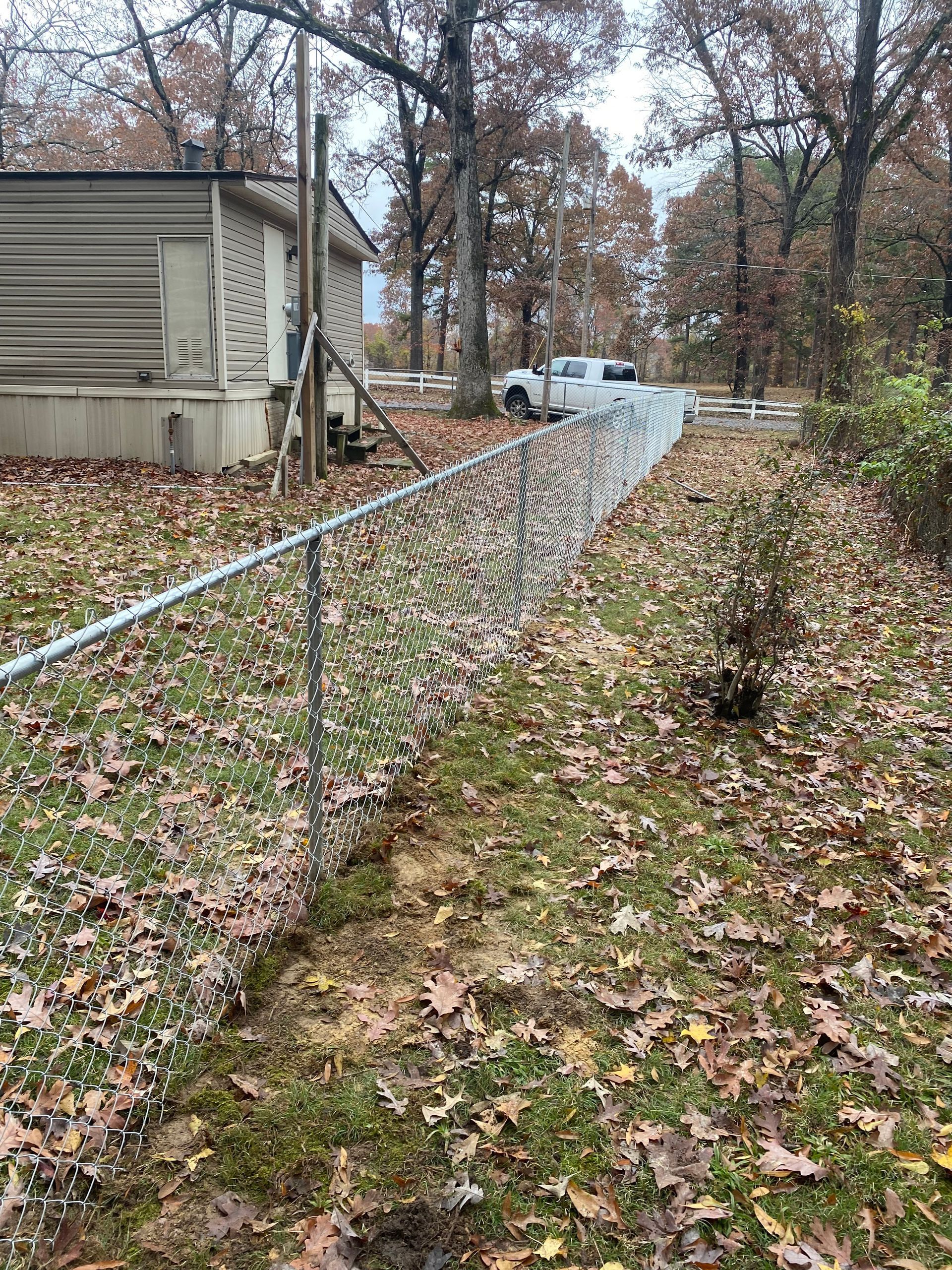 Chain-link fence in front yard with fallen leaves and a truck parked in the distance.