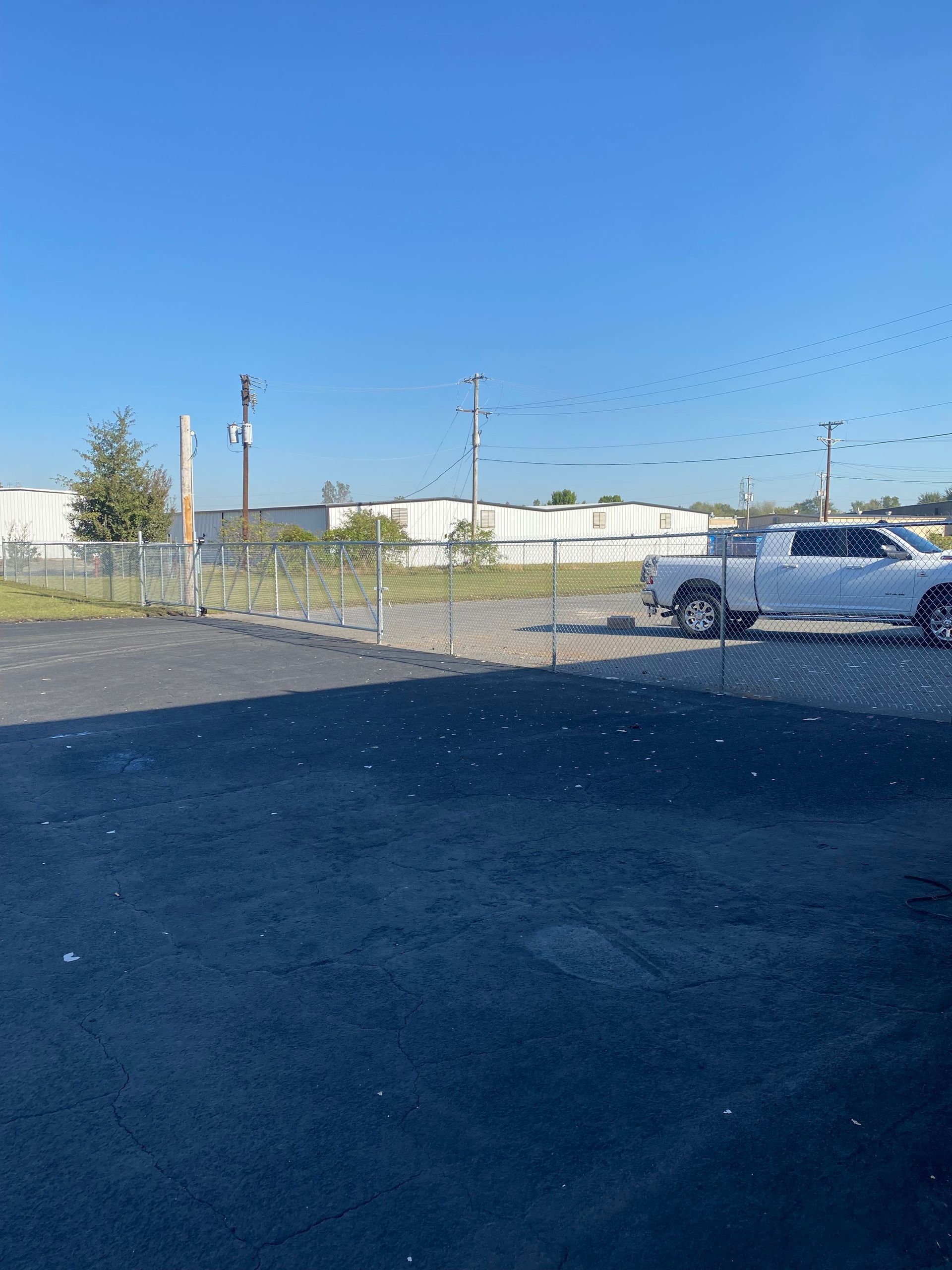 White pickup truck parked near a chain-link fence, industrial buildings in the background, blue sky.