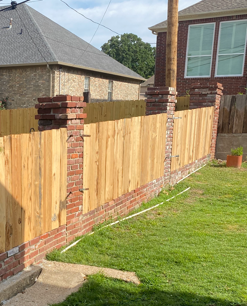 Wooden fence with brick columns and a lawn.