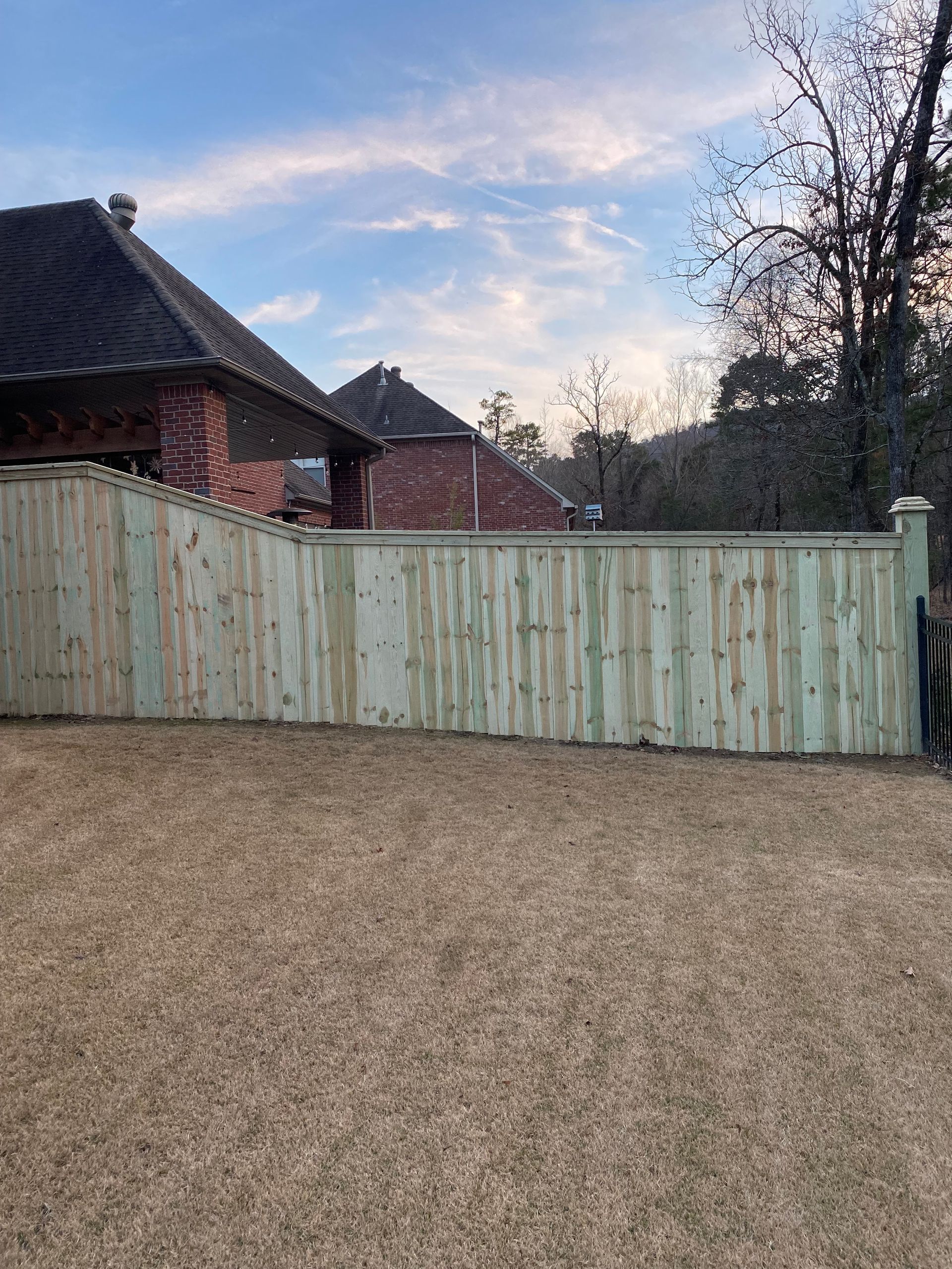 Barbed wire fence surrounding a grassy field with structures in the background, blue sky.