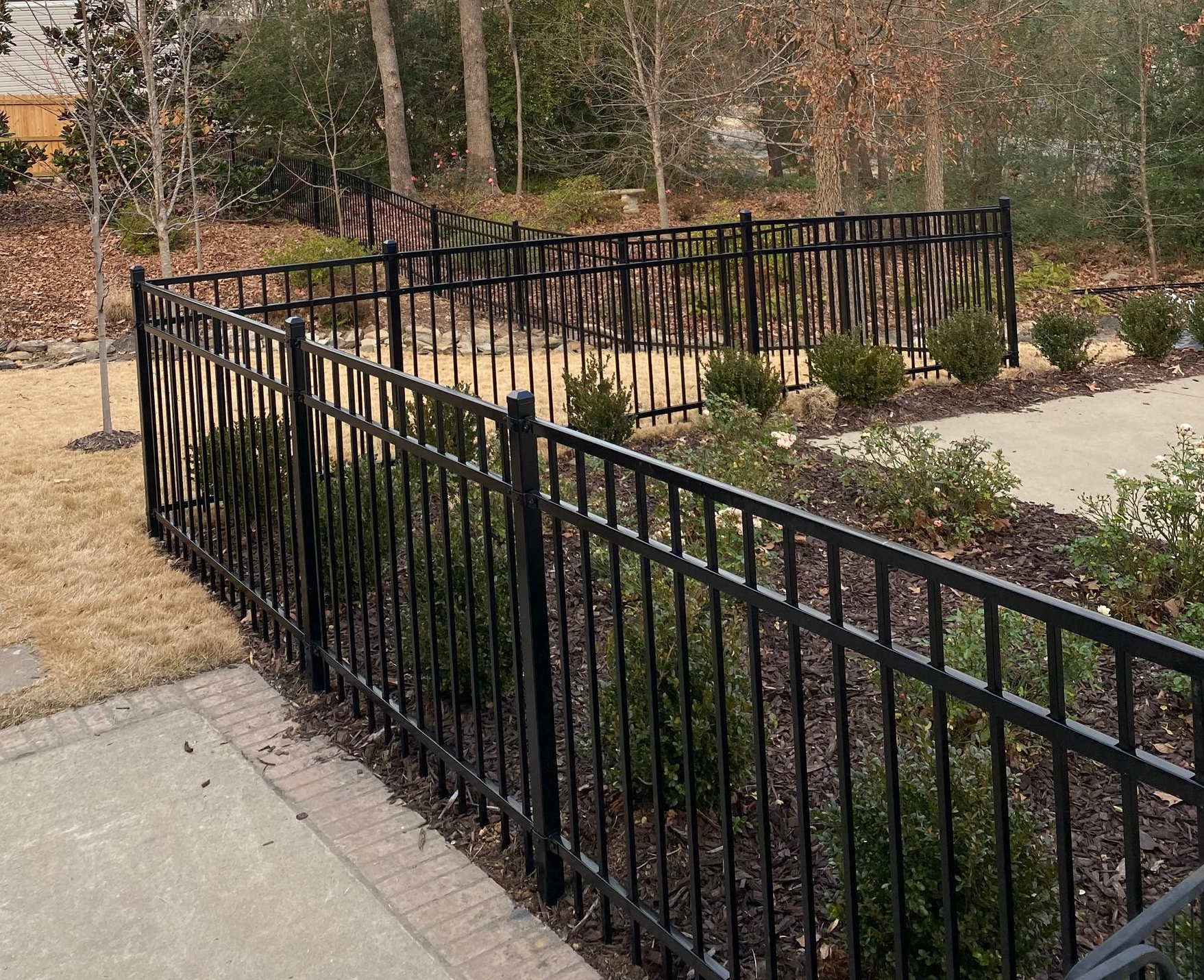 Black metal fence surrounding a garden bed with greenery.