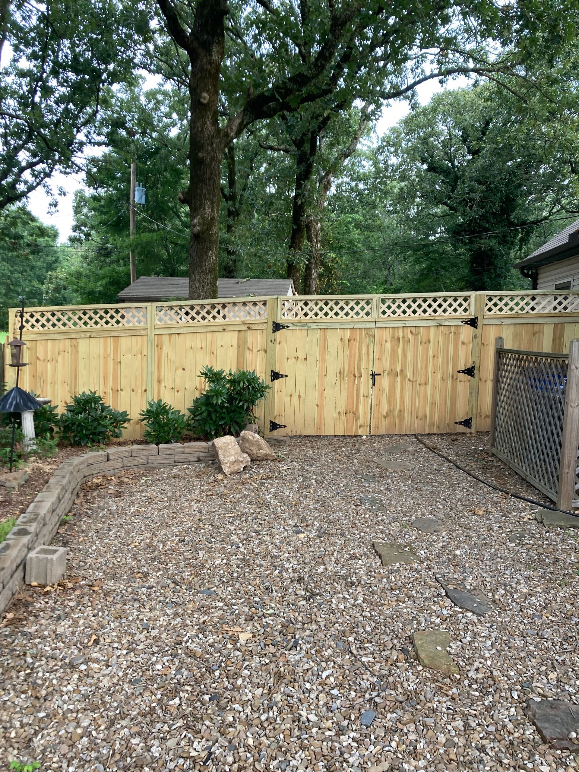 Wooden fence with gate, gravel yard, and trees in background.