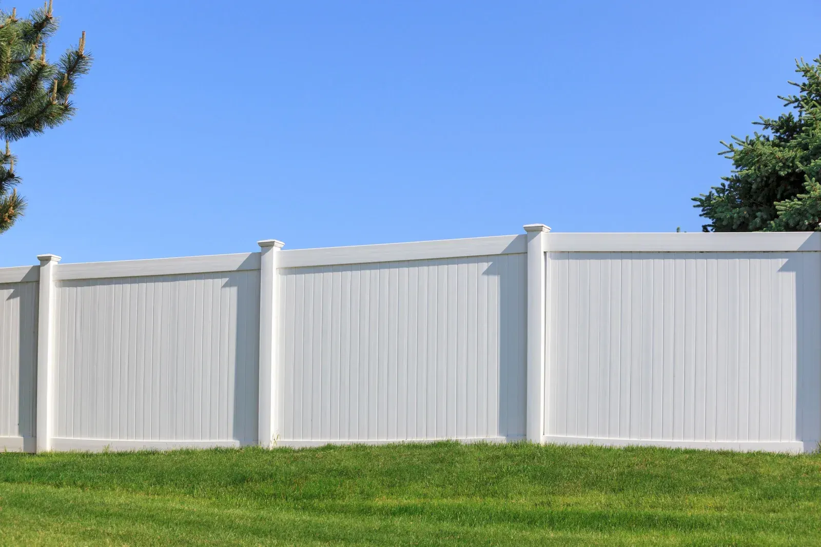 White vinyl fence in front of green grass under a clear blue sky.