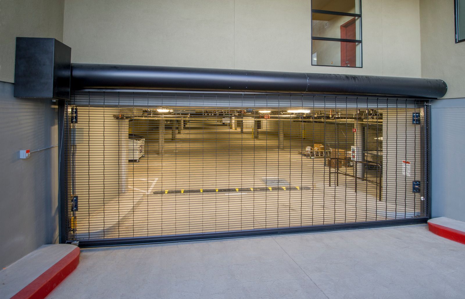 Rolling security gate open, revealing an empty parking structure. Black metal gate, tan building exterior.