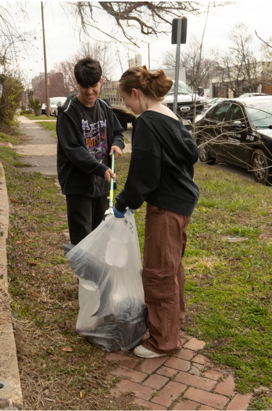 A man and a woman are picking up trash on the sidewalk.