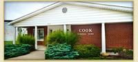 Exterior of the Cook Funeral Home with red brick and white siding. Bushes and walkway in front.