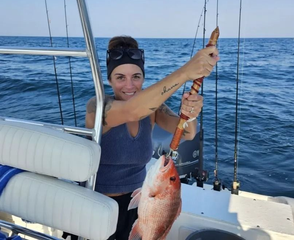 A person holding a red snapper fish caught on a boat while out at sea.