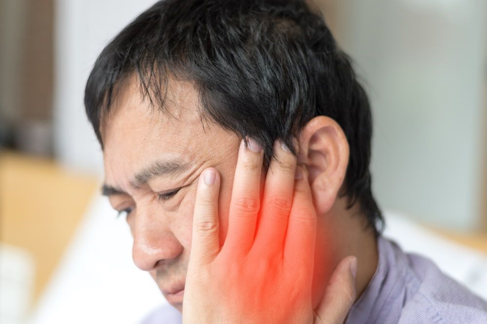 A Man is Holding His Face in Pain Because of a Toothache — New Horizons Dental in Port Douglas, QLD