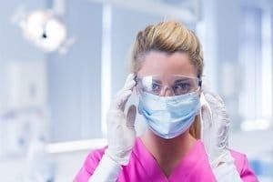 A Female Dentist Wearing a Mask and Goggles in an Operating Room — New Horizons Dental in Port Douglas, QLD