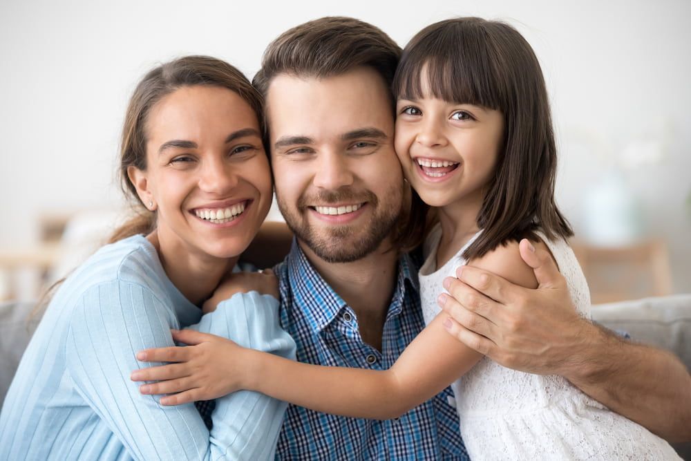A Family is Posing for a Picture While Sitting on a Couch — New Horizons Dental in Port Douglas, QLD