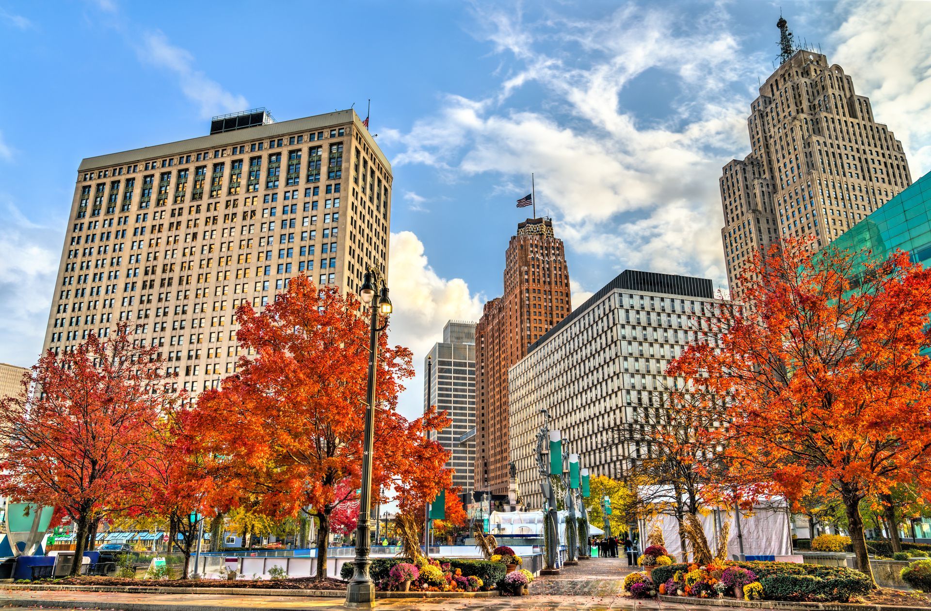 Autumn city park with red-orange trees and tall downtown buildings under a blue sky